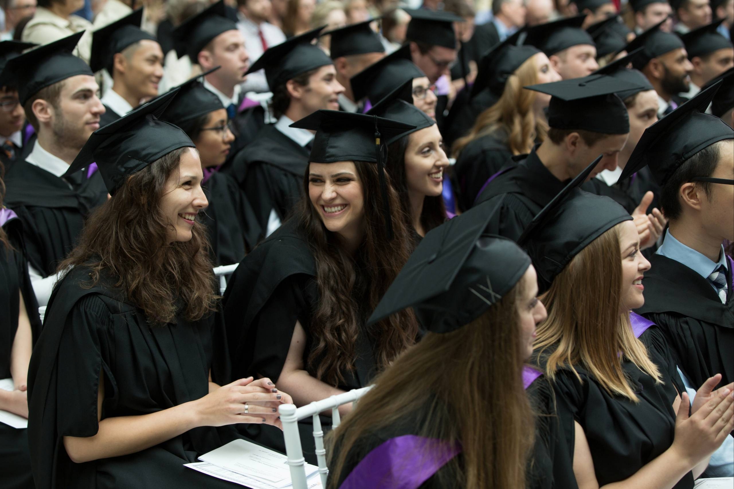 A group of graduating students in caps and gowns smile and clap at Bannatyne Convocation.
