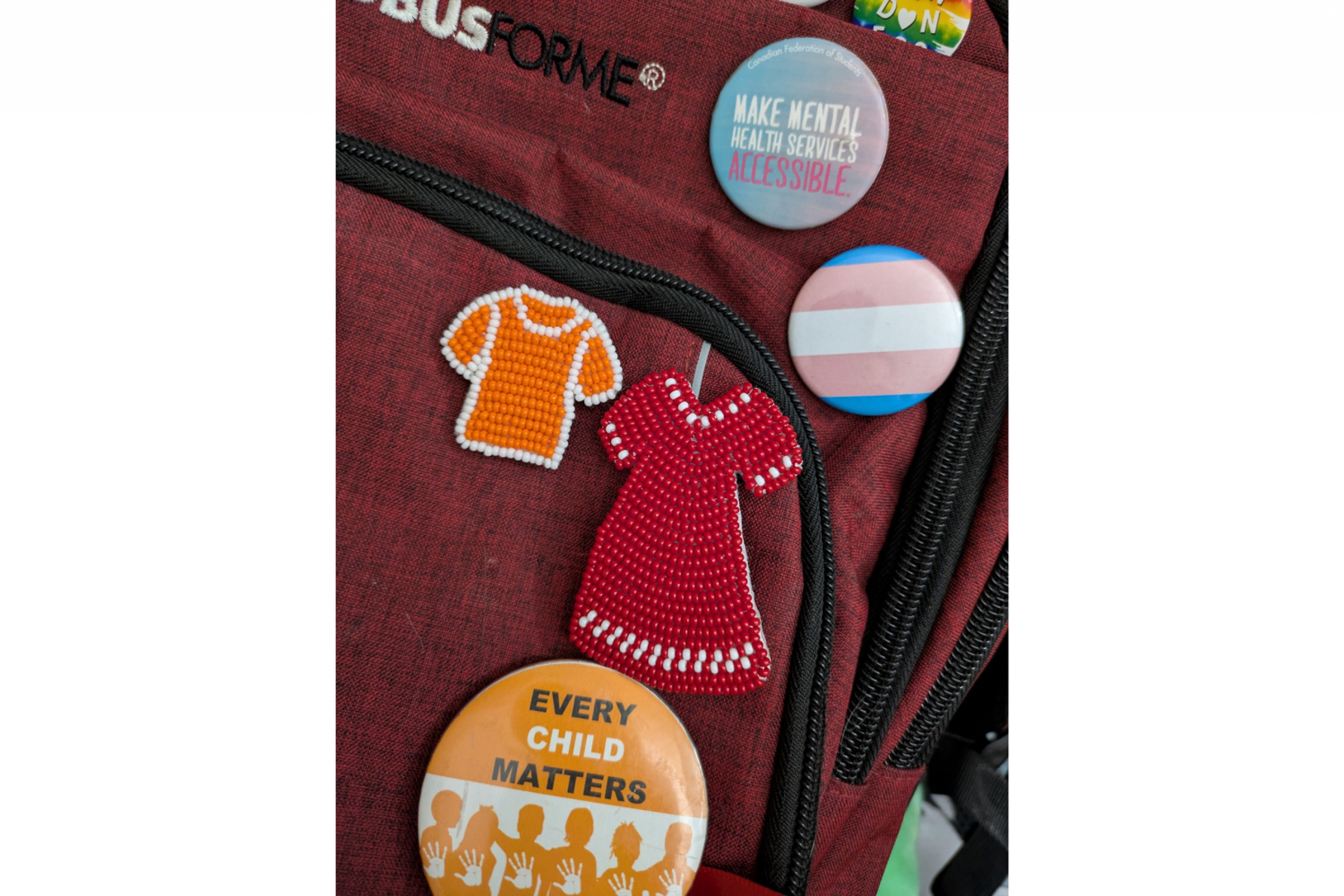Beaded red dress and orange shirt pins and an assortment of classic button pins on a back pack