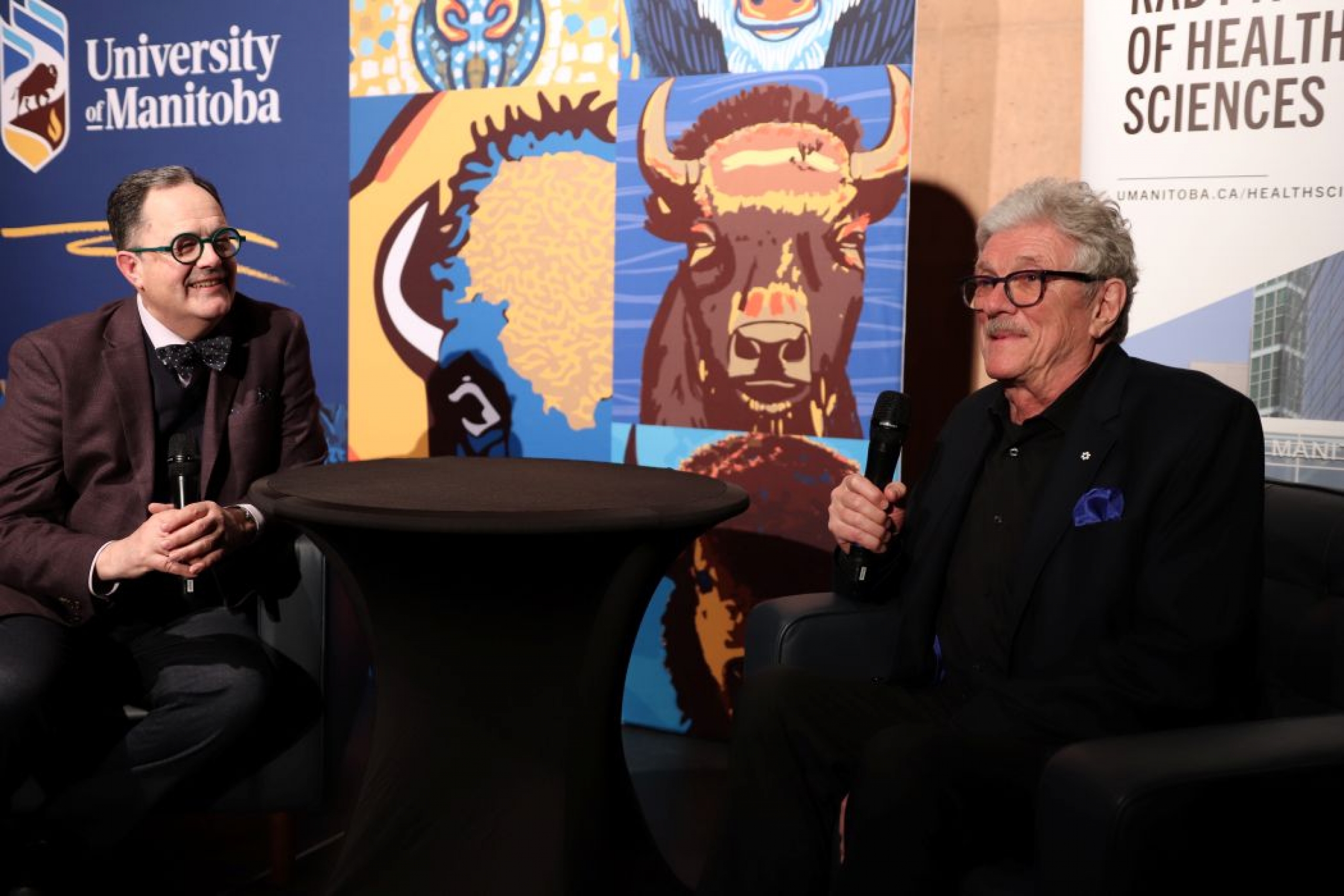 Two people are seated. They are both holding microphones. 