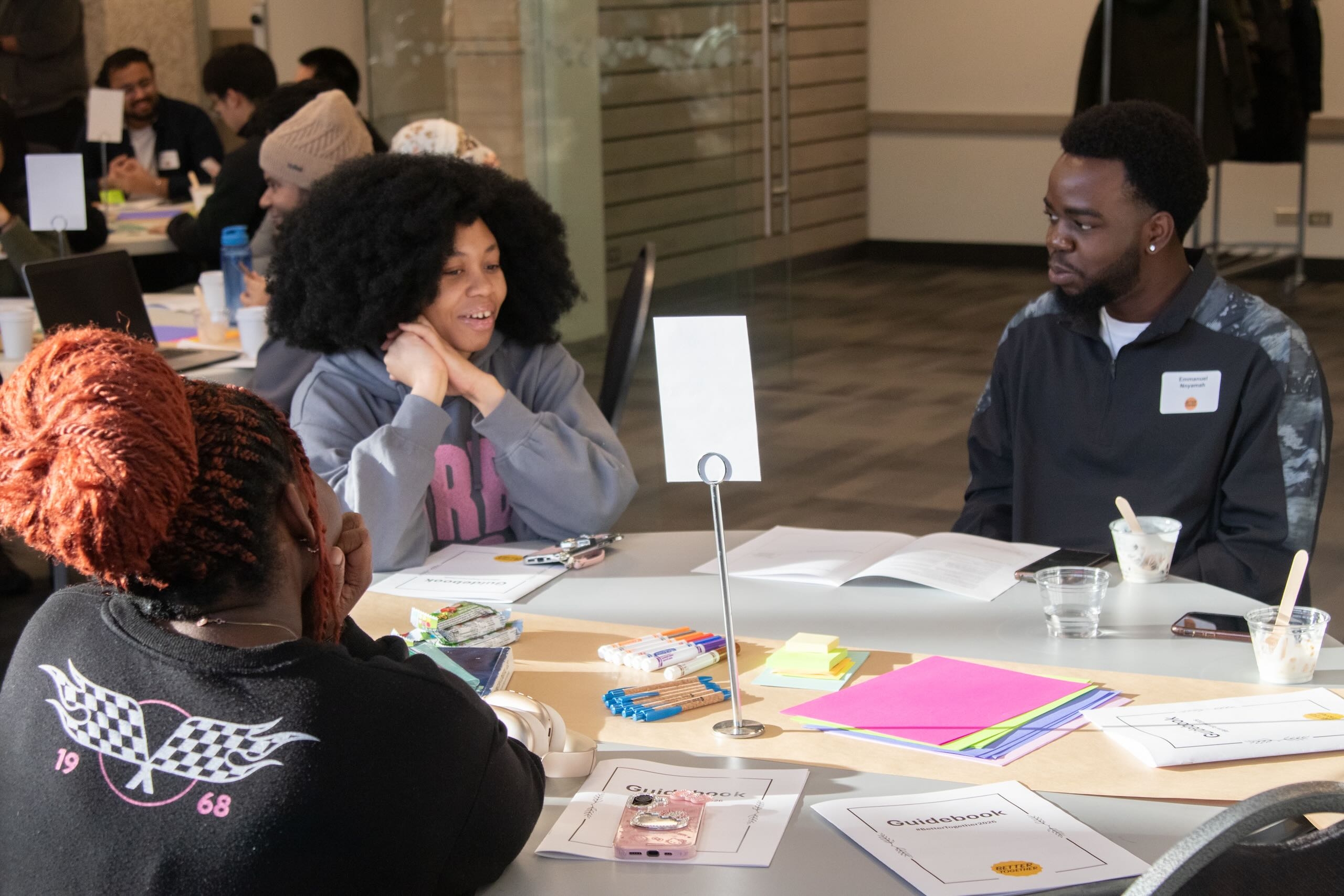 Three people sitting at a table with paper, pens and booklets scattered across.