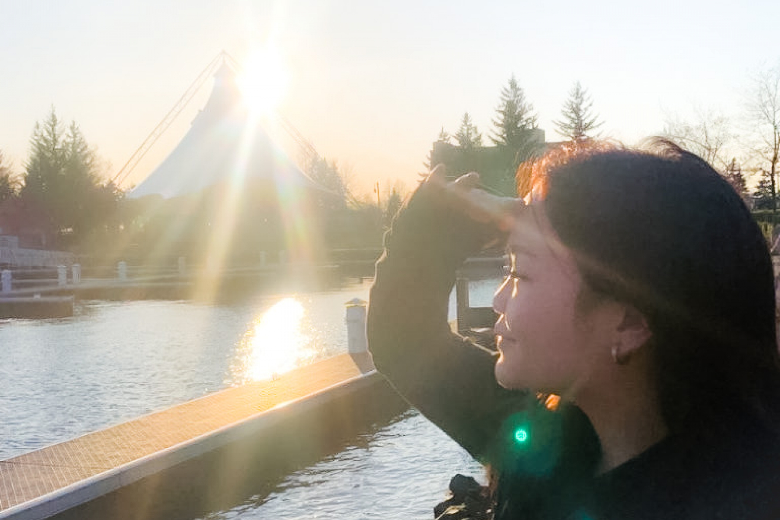 A person looking out over a body of water with a sunset behind a large tent in the background.