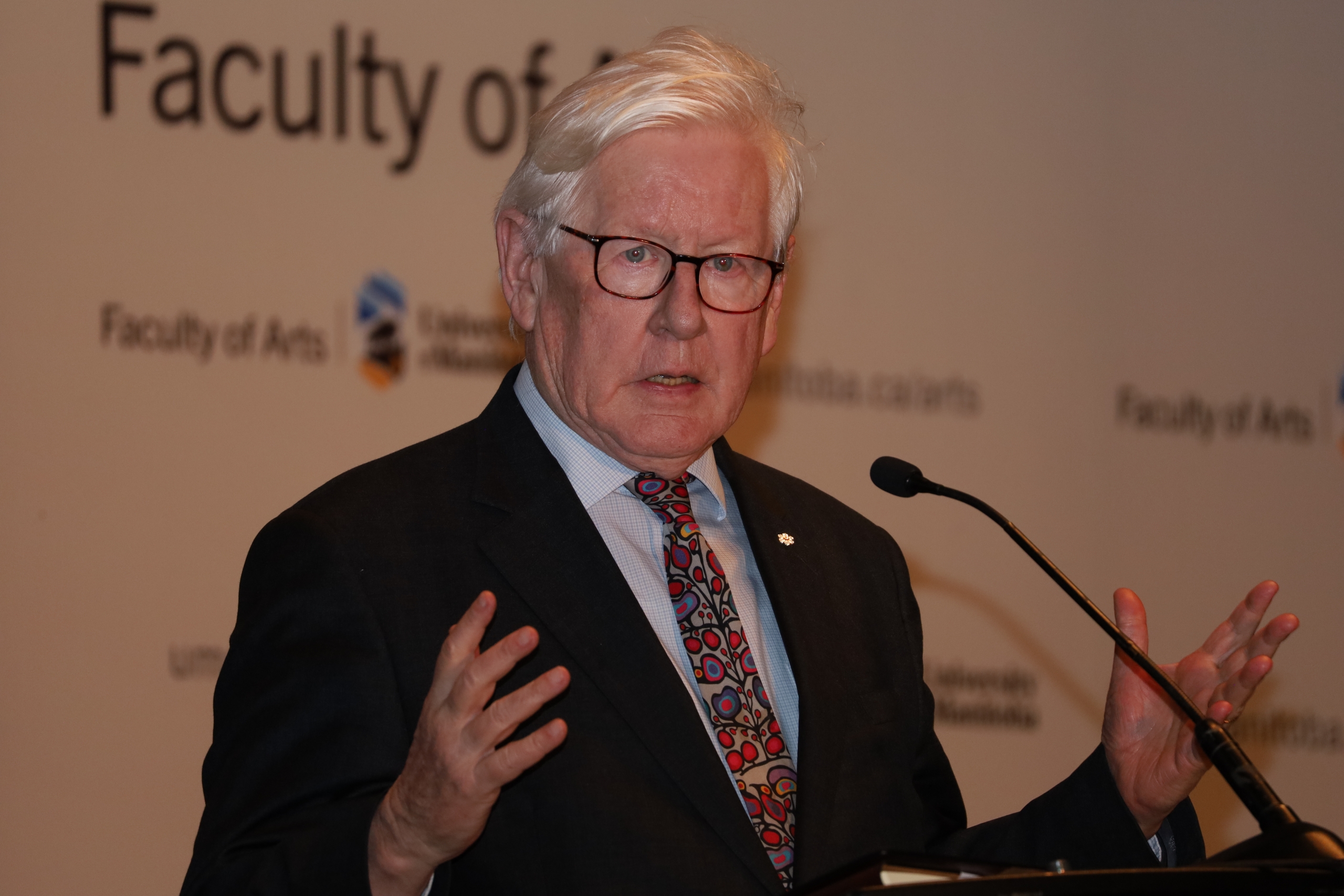 Bob Rae standing at a podium with microphone, addressing a crowd.