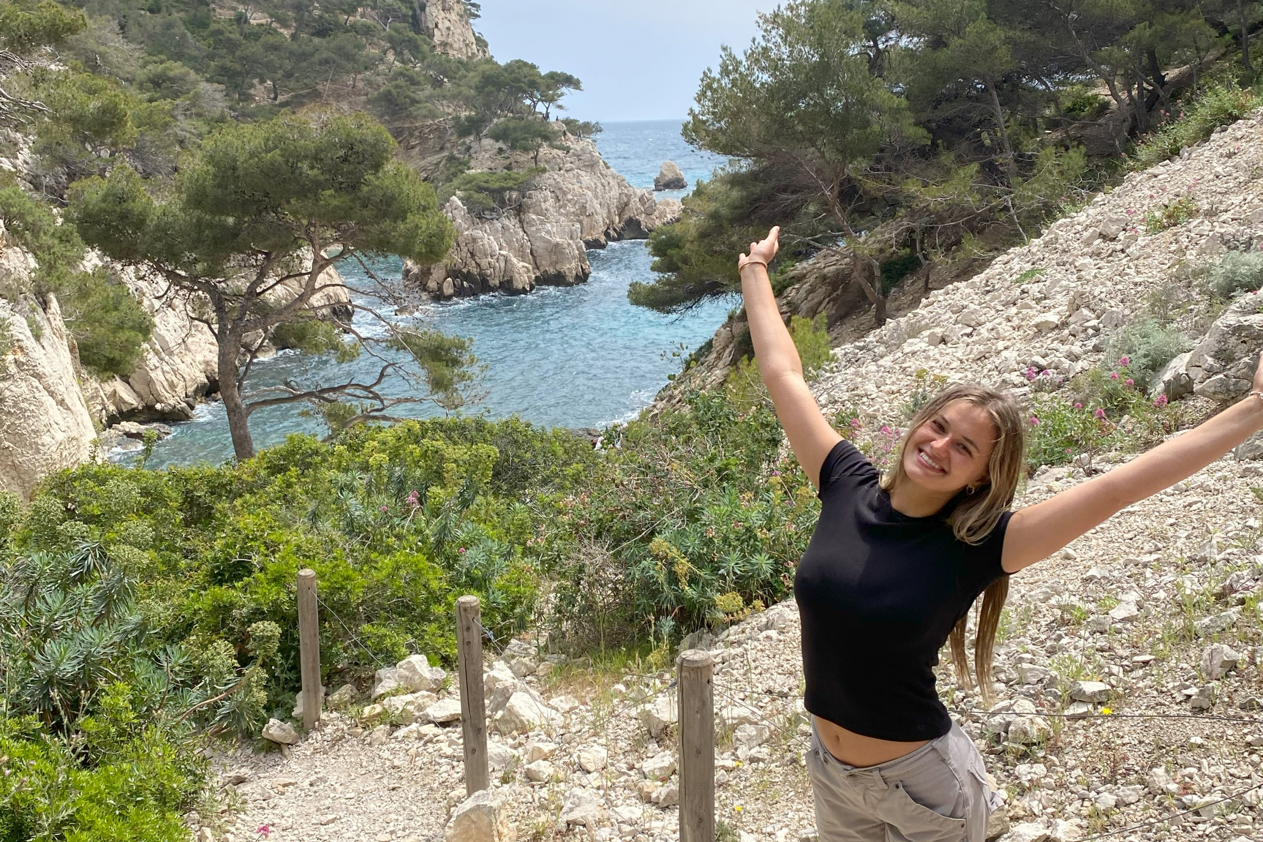 Brooke poses with her arms up by a rocky beach area