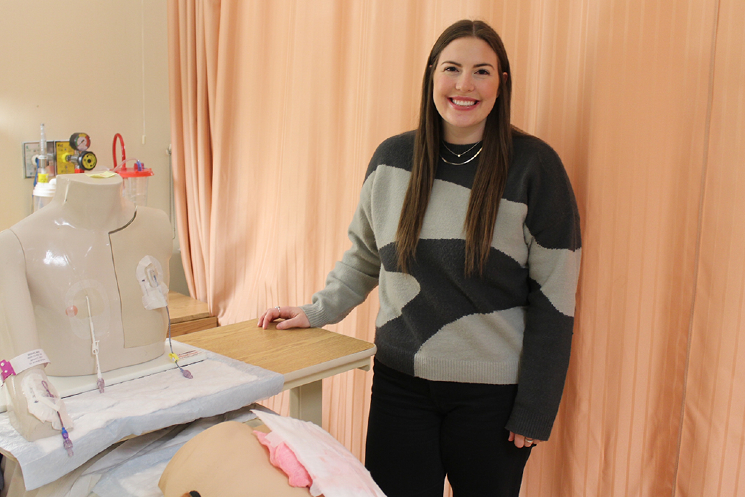 A nursing student posing at a simulation lab bedside.