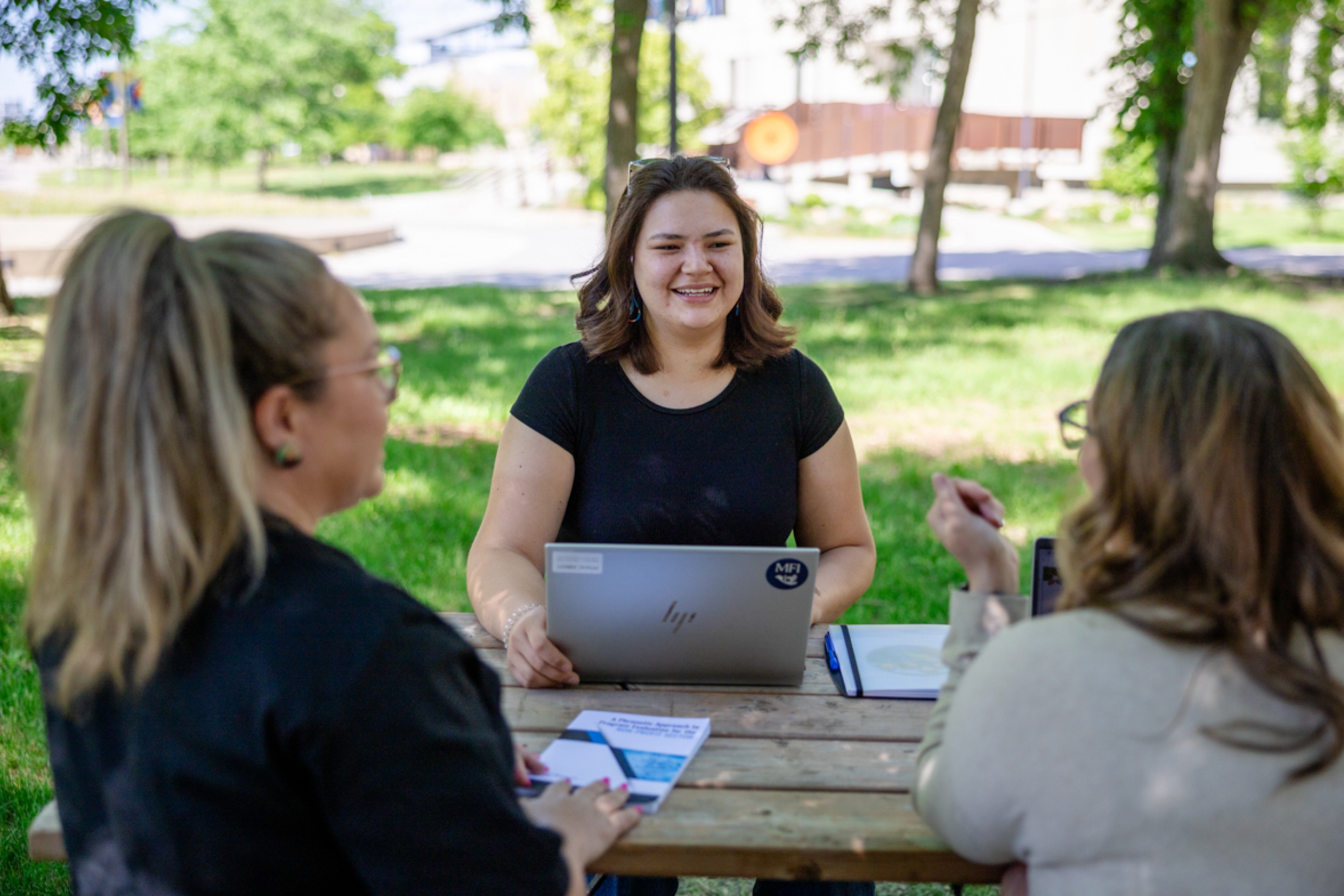 Three students sitting outdoors on a picnic table.