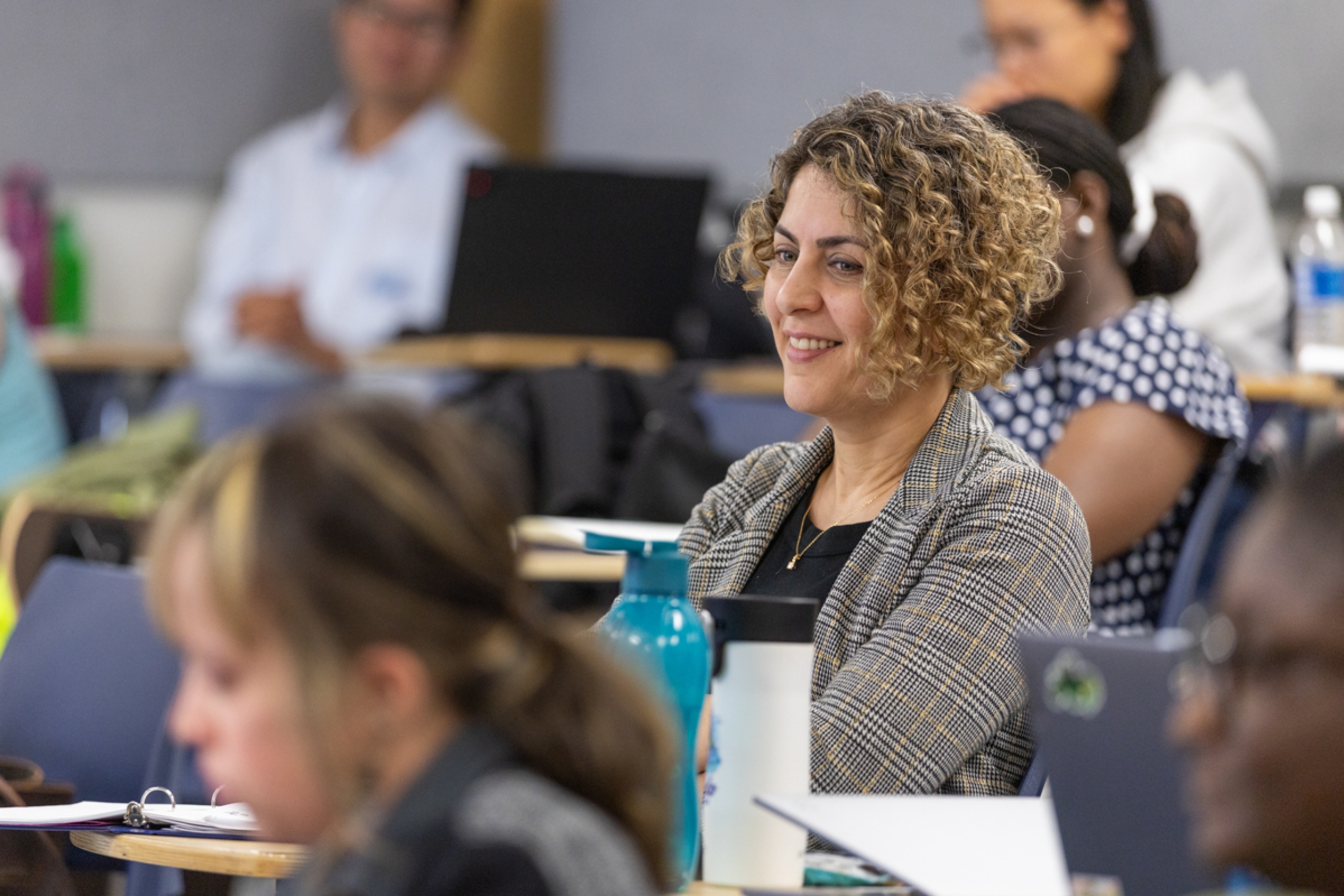 Students listening in a classroom, focusing on one smiling student.