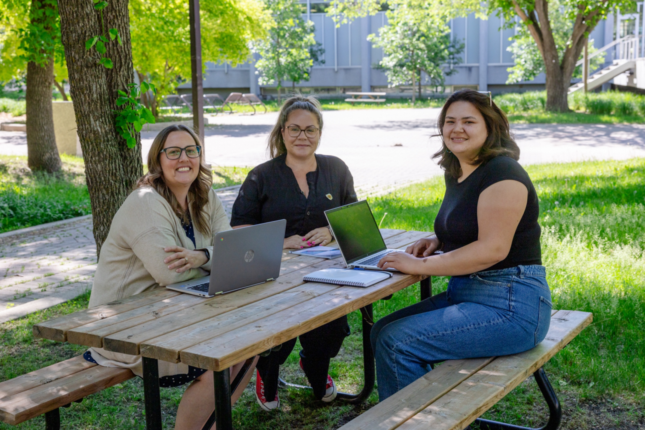 Three students sitting on a picnic bench.
