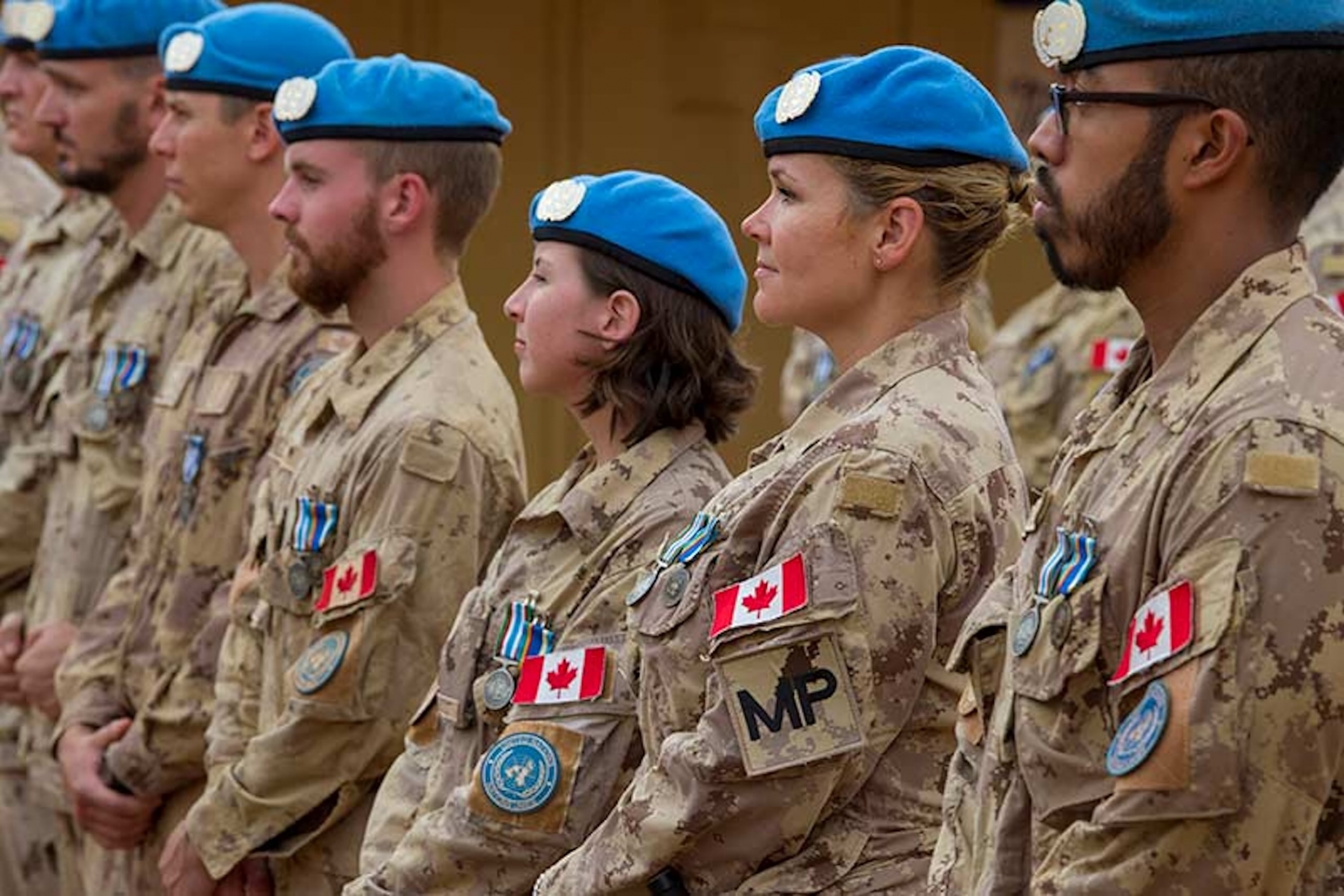 side profile of a row of 7 Canadian Armed Forces members wearing blue United Nations berets.