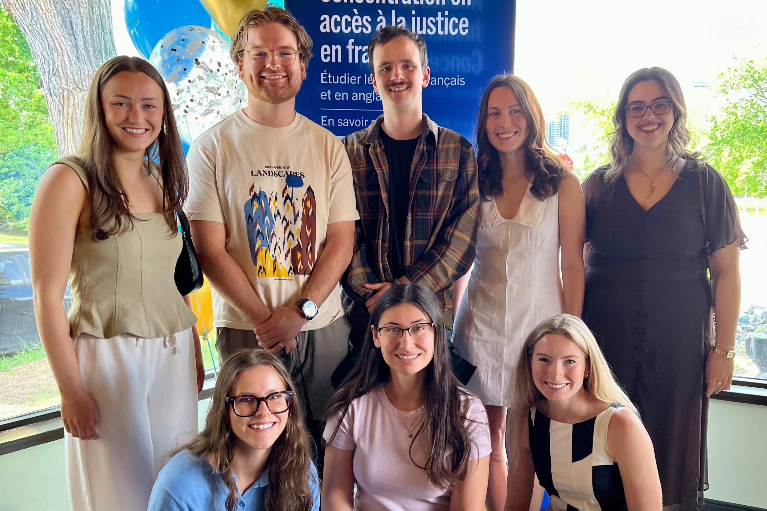 eight smiling students in casual dress stand in front of a sign that says access to justice in French