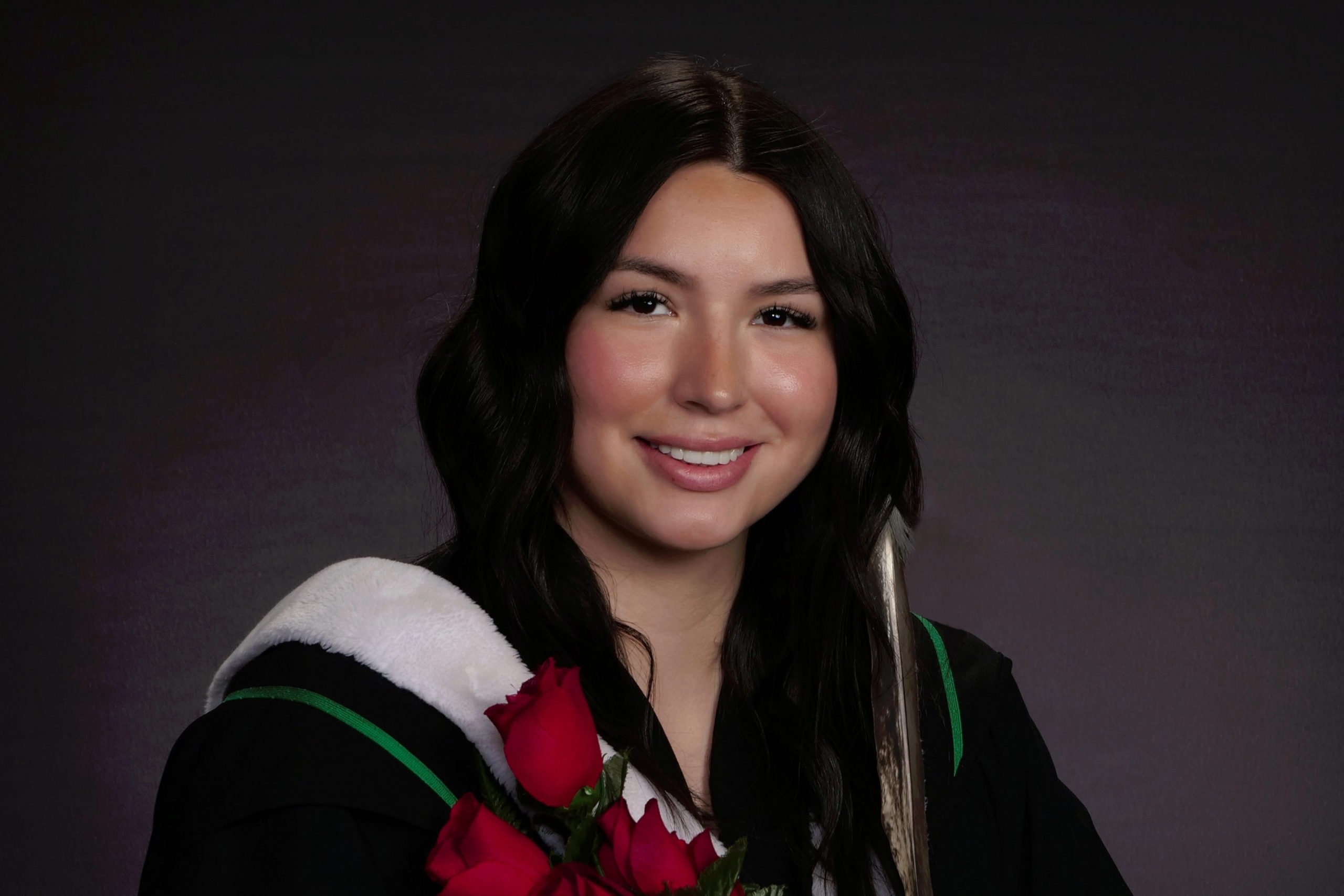 a woman in a graduation gown holds roses and smiles
