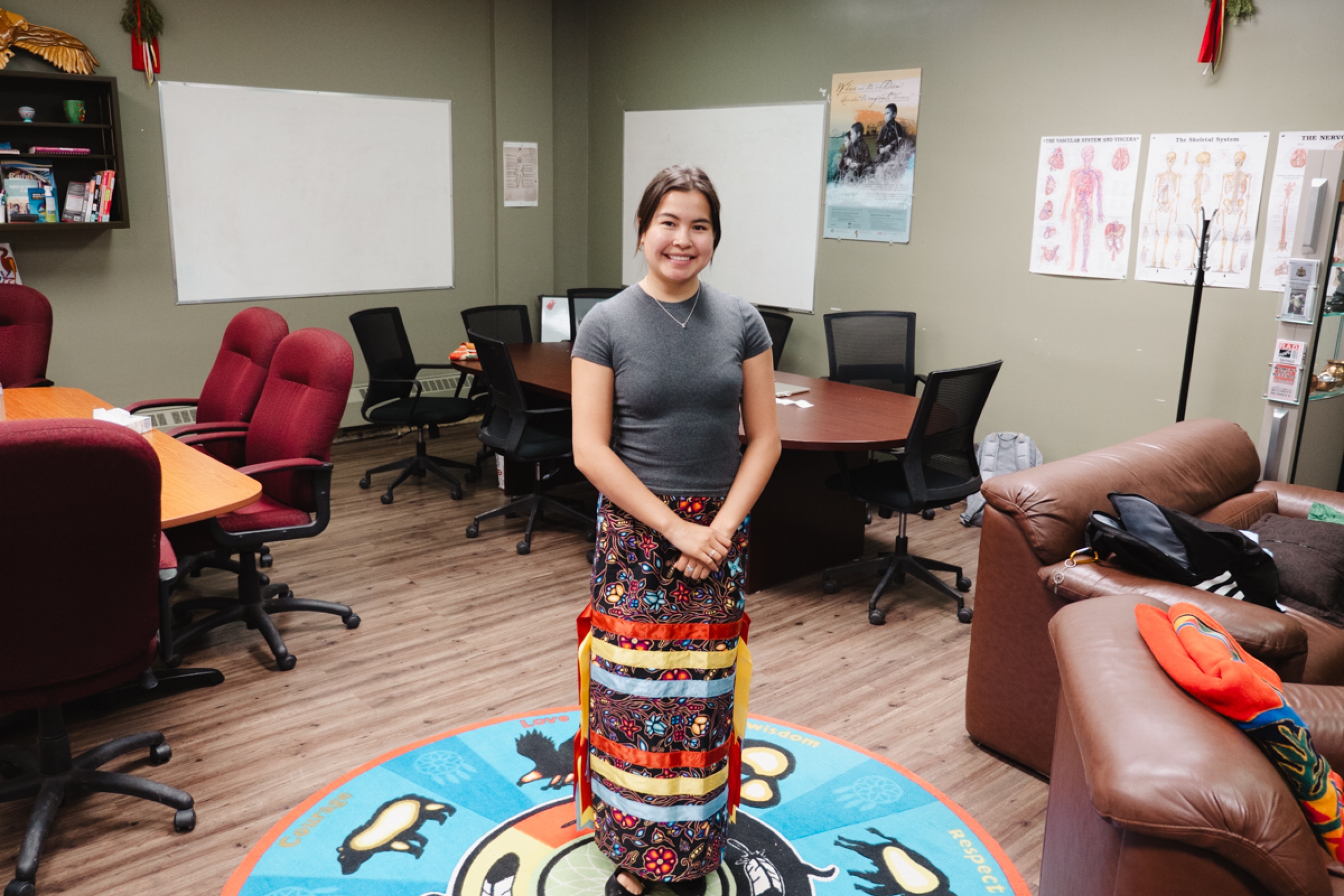 A person standing in the middle of a room. She stands on a mat that has words: Courage, Love Wisdom and Respect.