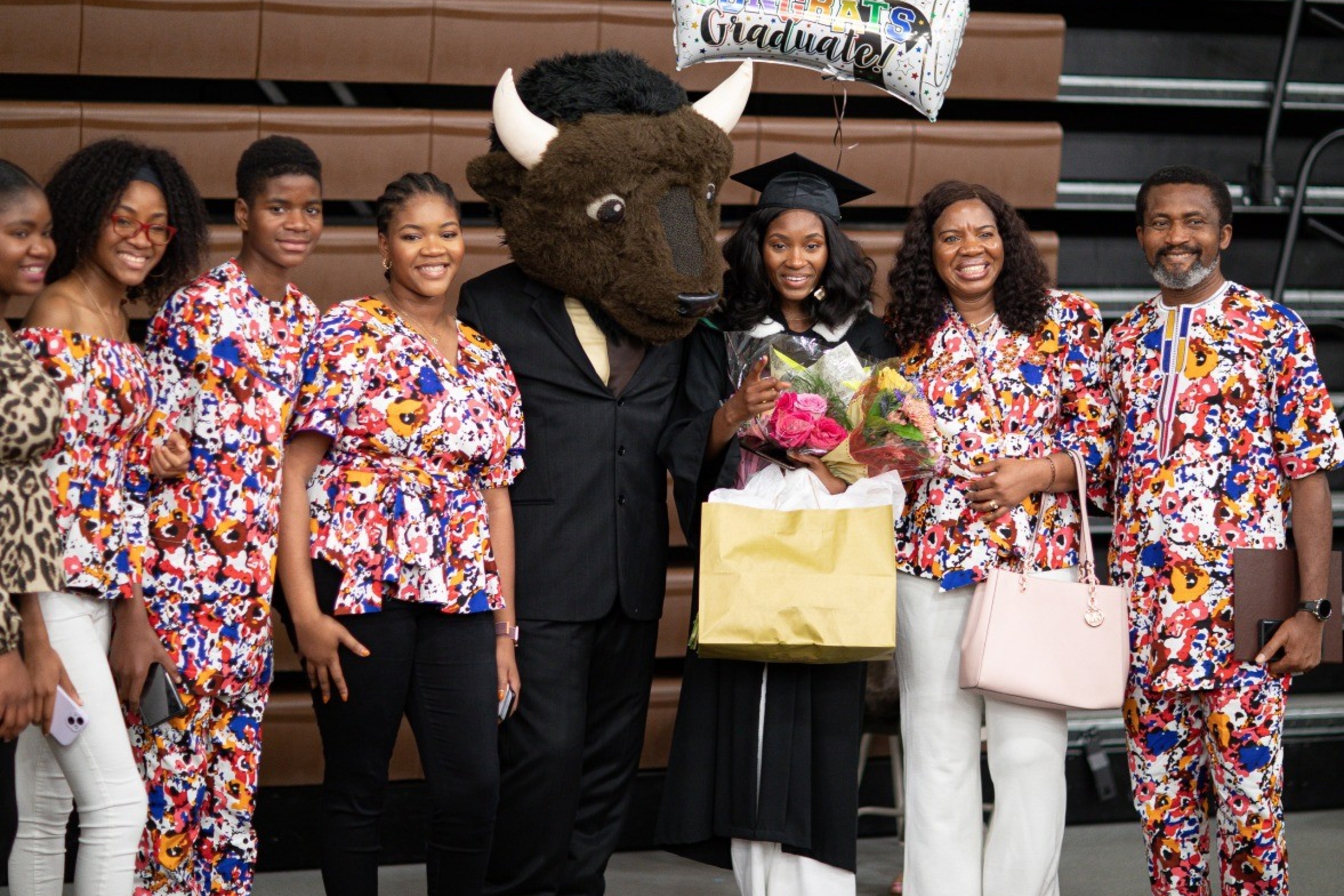 A family in brightly coloured clothing poses with their grad and Billy, UM's mascot.