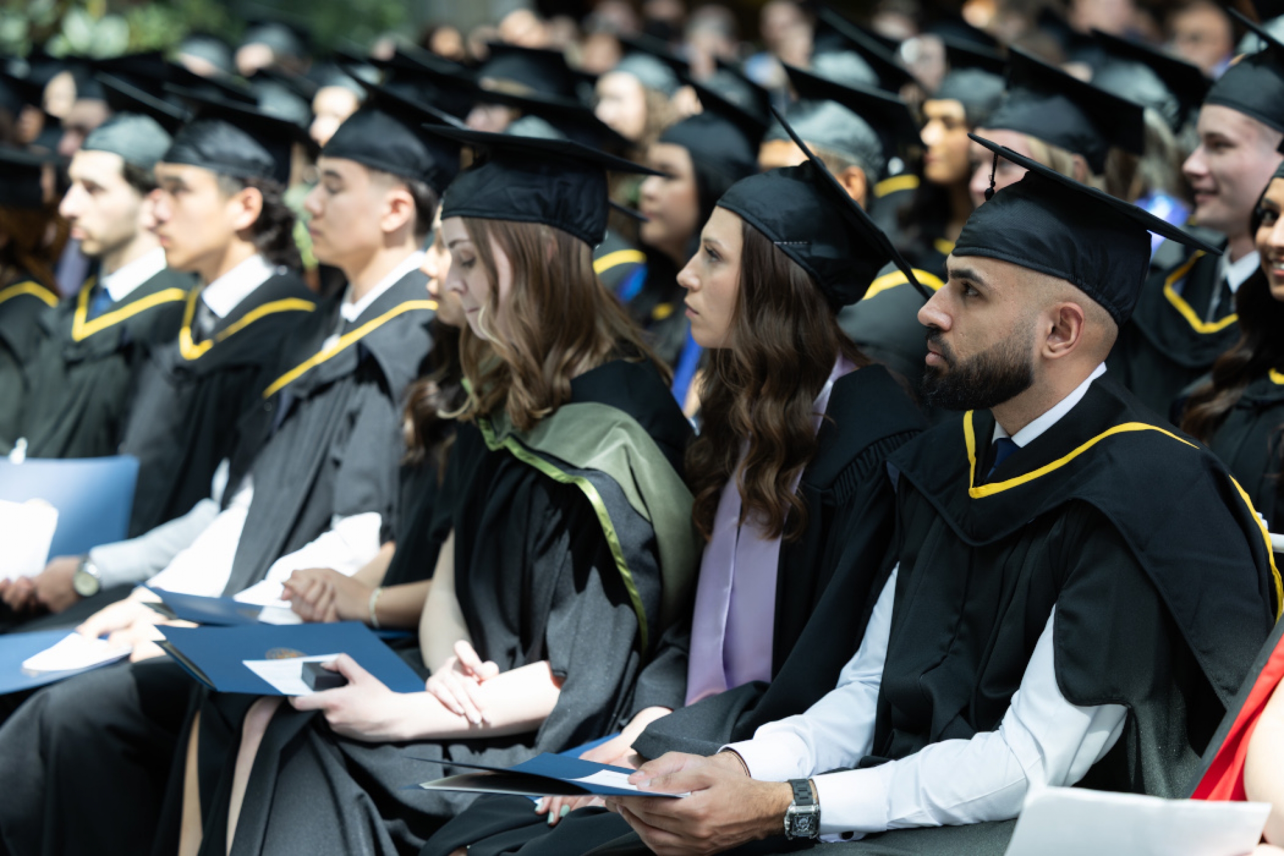 Three rows of students are seated and are wearing caps and gowns.