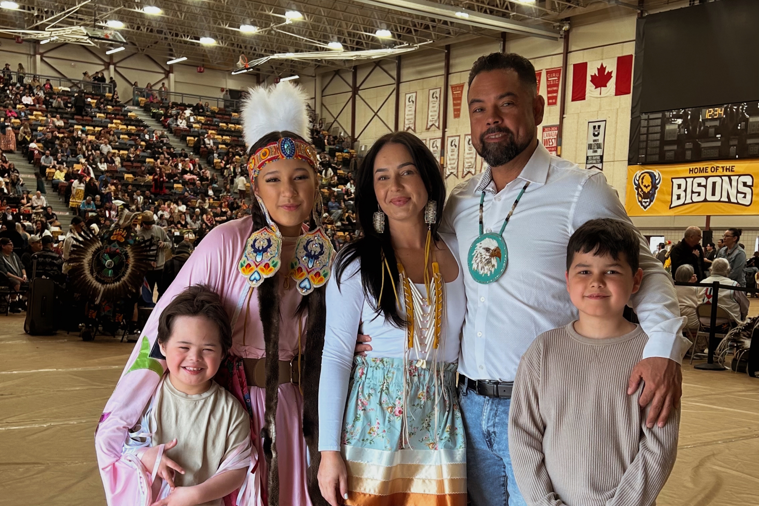 Courtney Chartrand wearing a ribbon skirt and surrounded by family members at a pow wow.