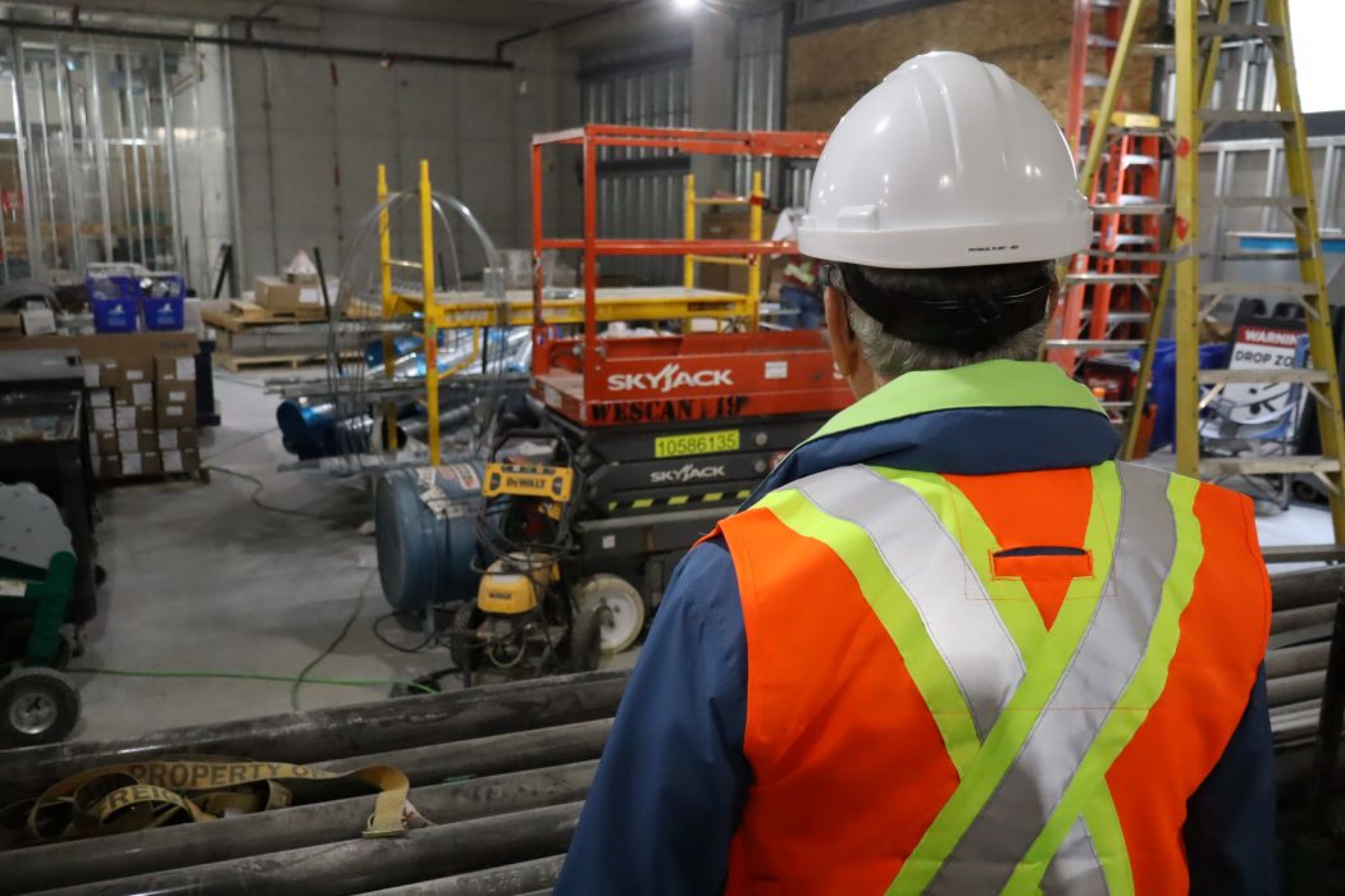 A person wearing a hard hat and high vis vest looks over a construction area inside a building.