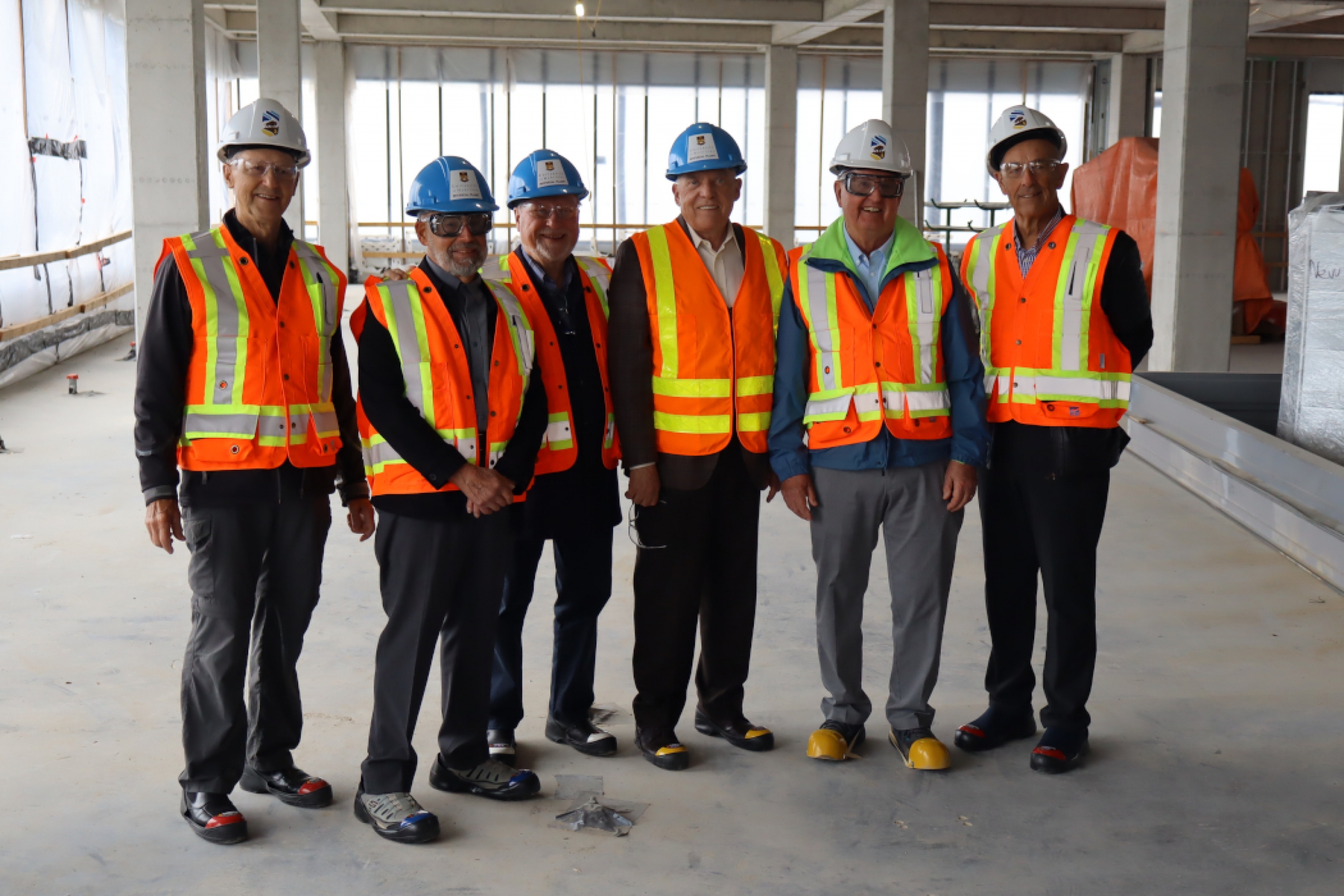 Six people wearing hard hats, safety glasses and high-vis vests in an interior construction area.