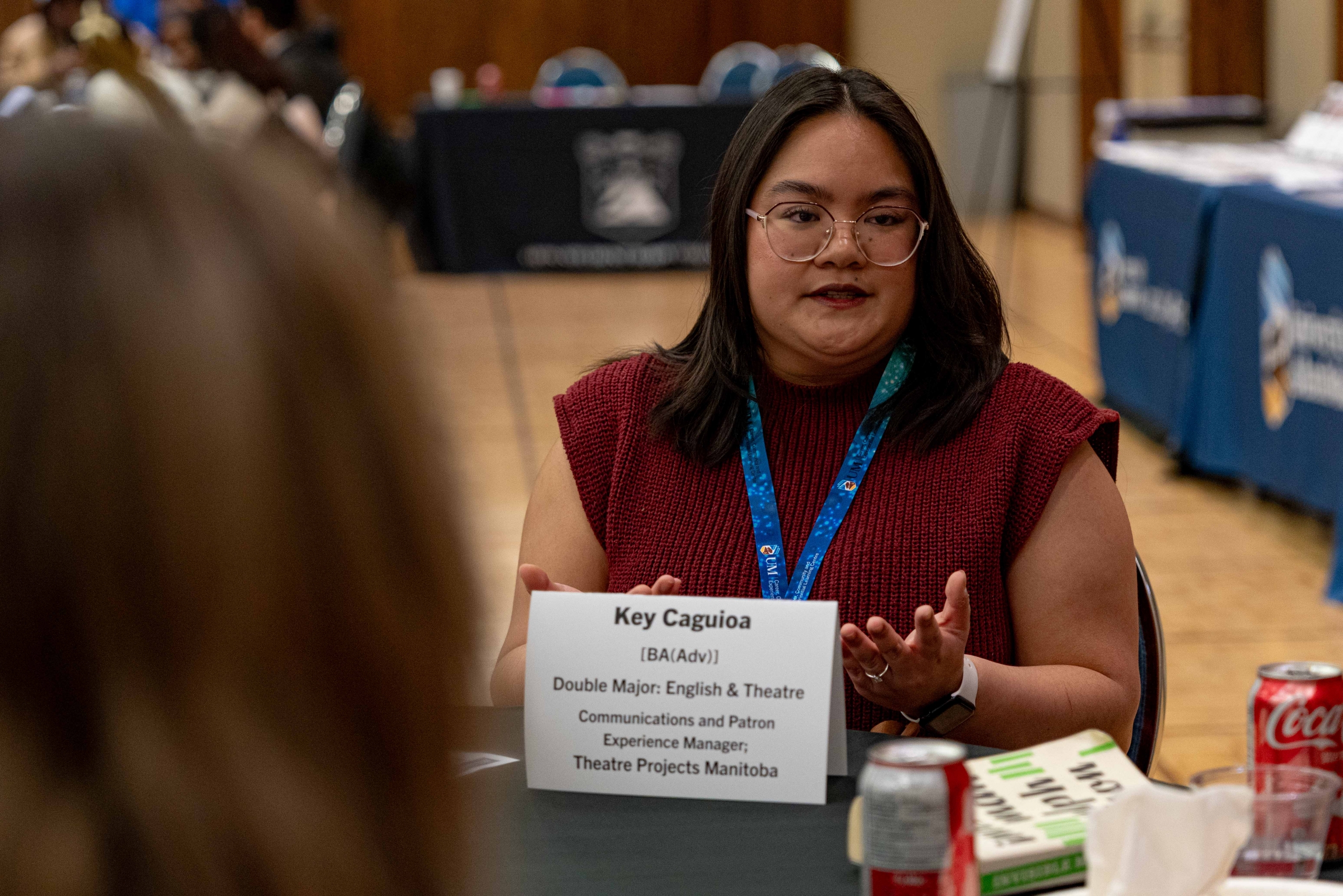 A woman sitting at a table, wearing a lanyard.
