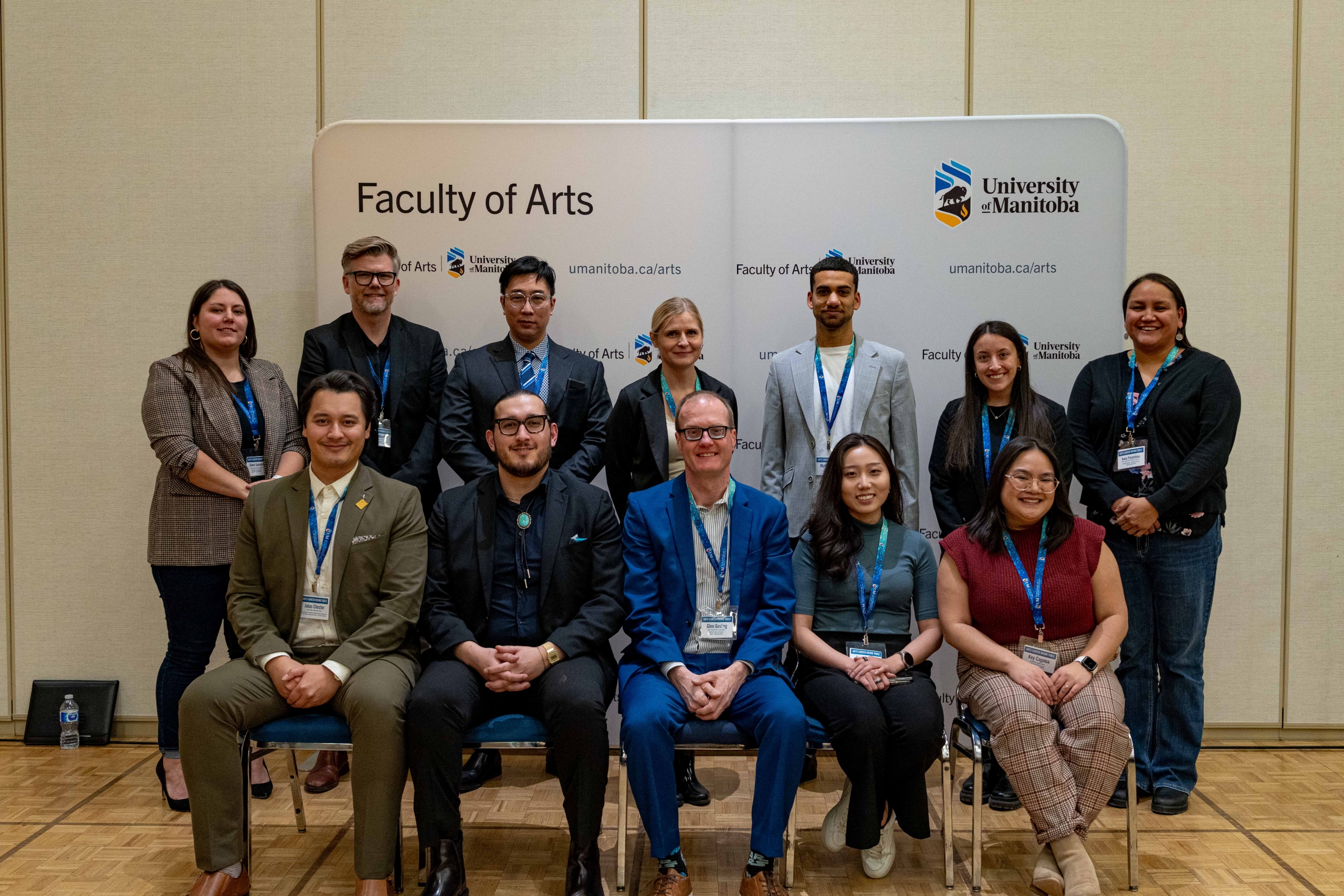 A group of twelve people posing in front of a Faculty of Arts banner.
