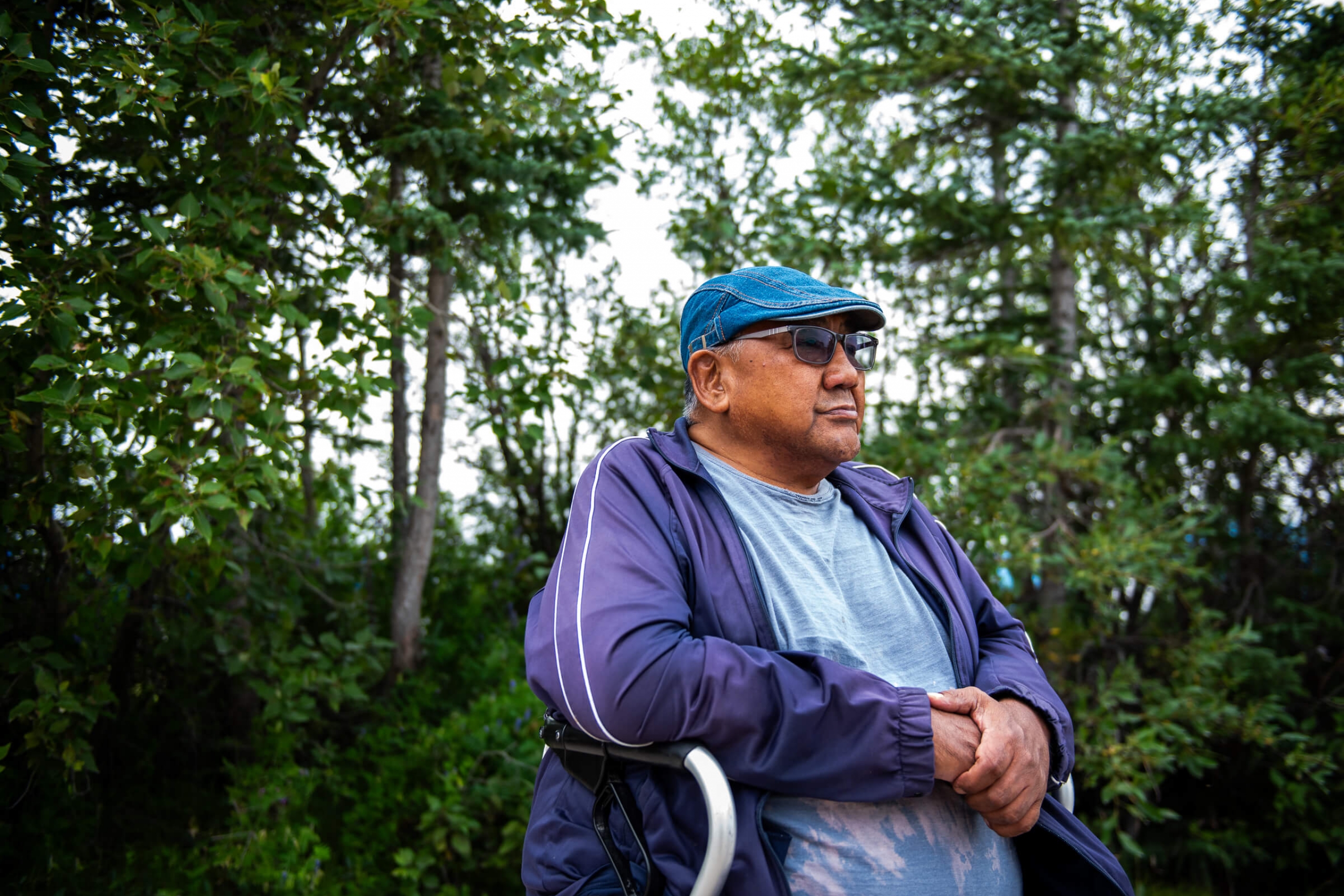 An older man sits in a walker with a forest in the background