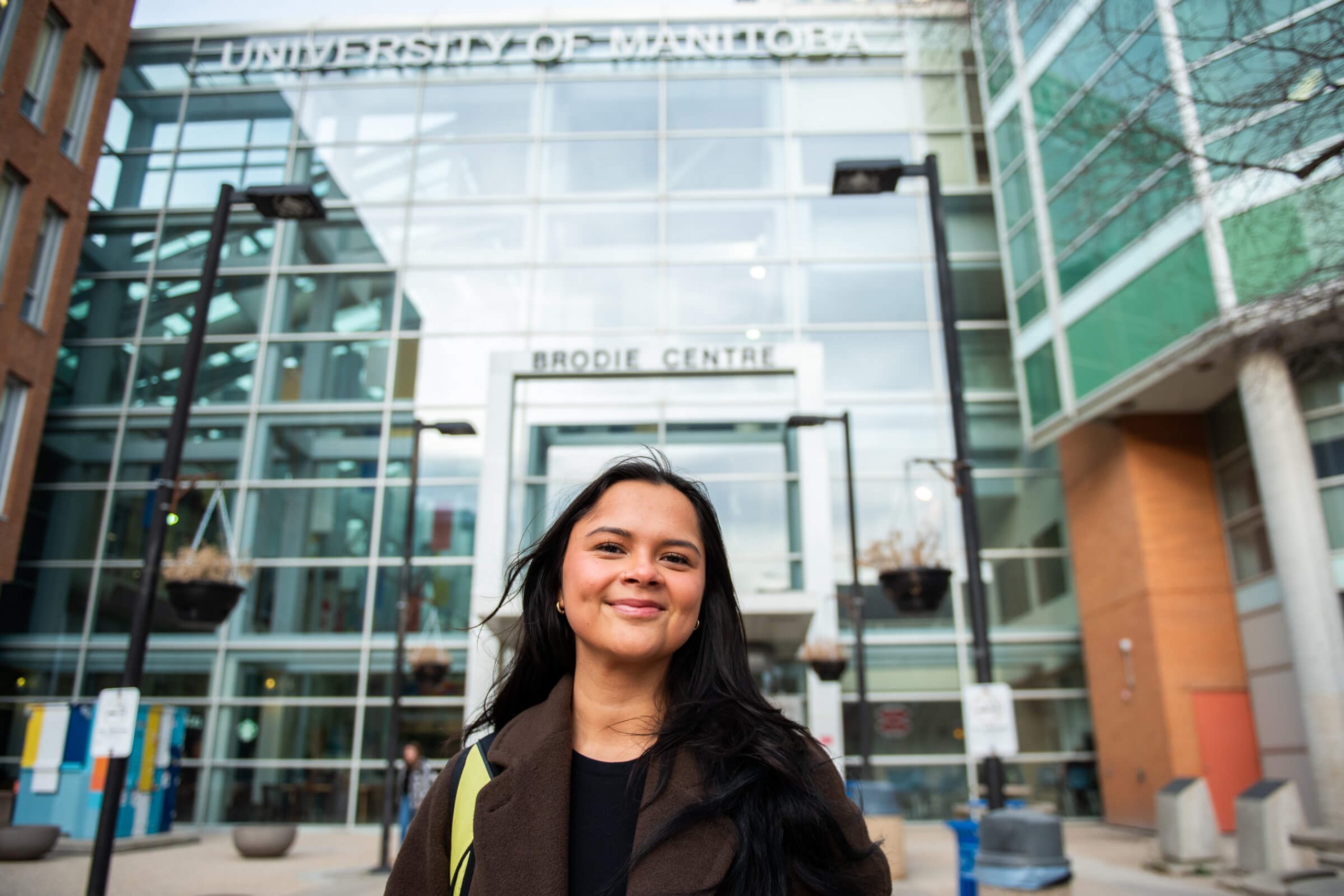 A smiling young woman in front of a University of Manitoba building