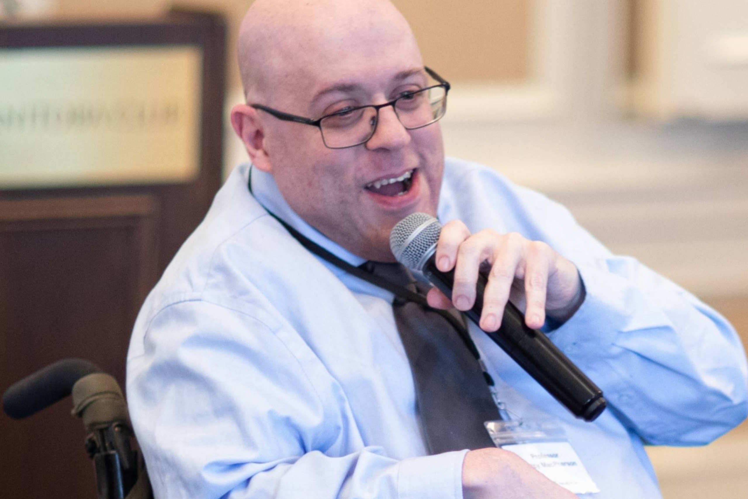 Smiling person in wheelchair speaks into mic