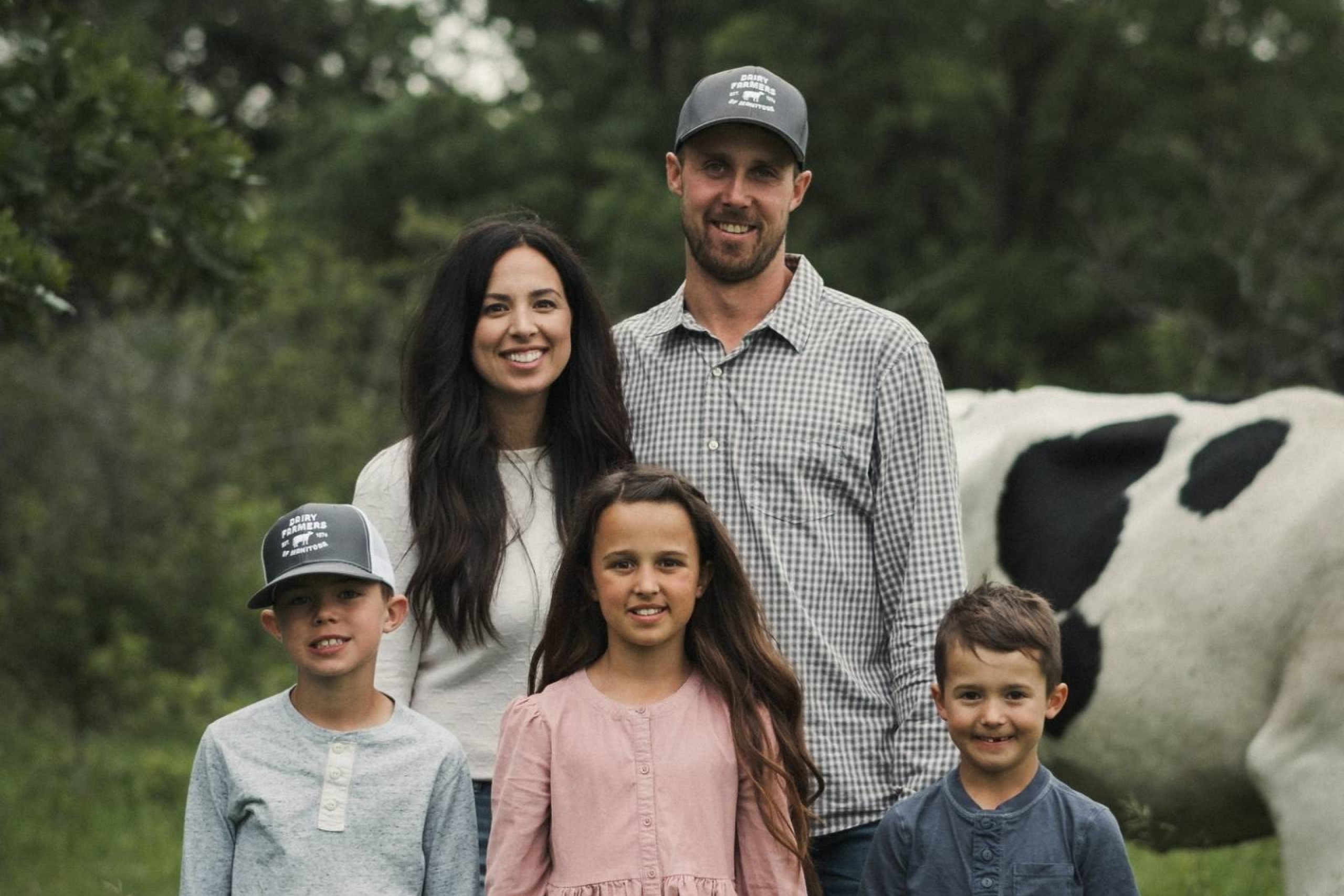 A family of five standing in front of a cow in a field.