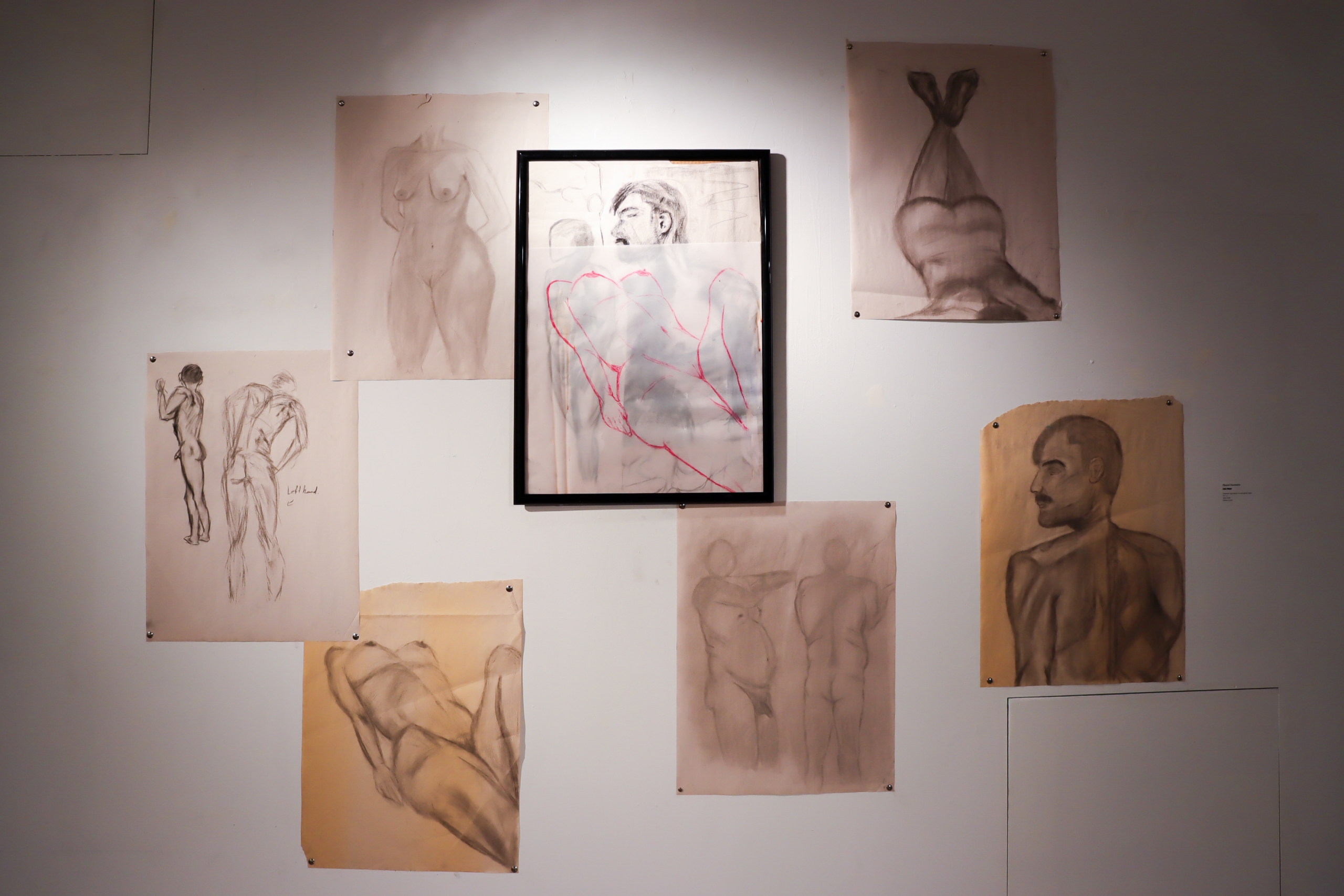 Installation view featuring figurative drawings arranged around a framed central artwork.