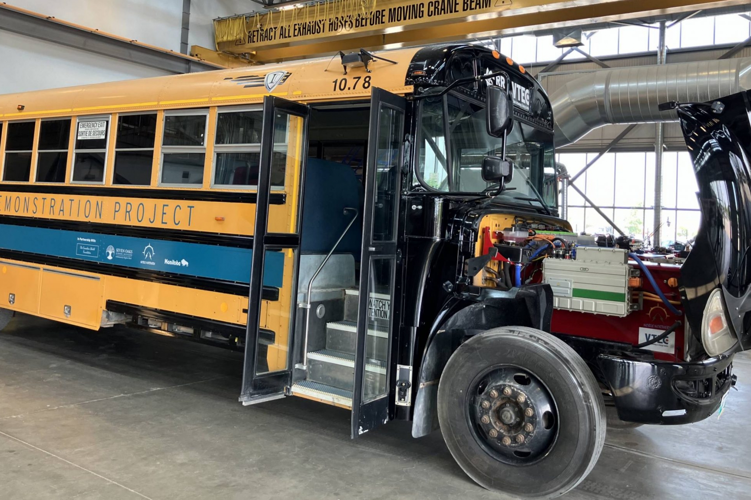 A school bus with the front hood up, showing an electric motor
