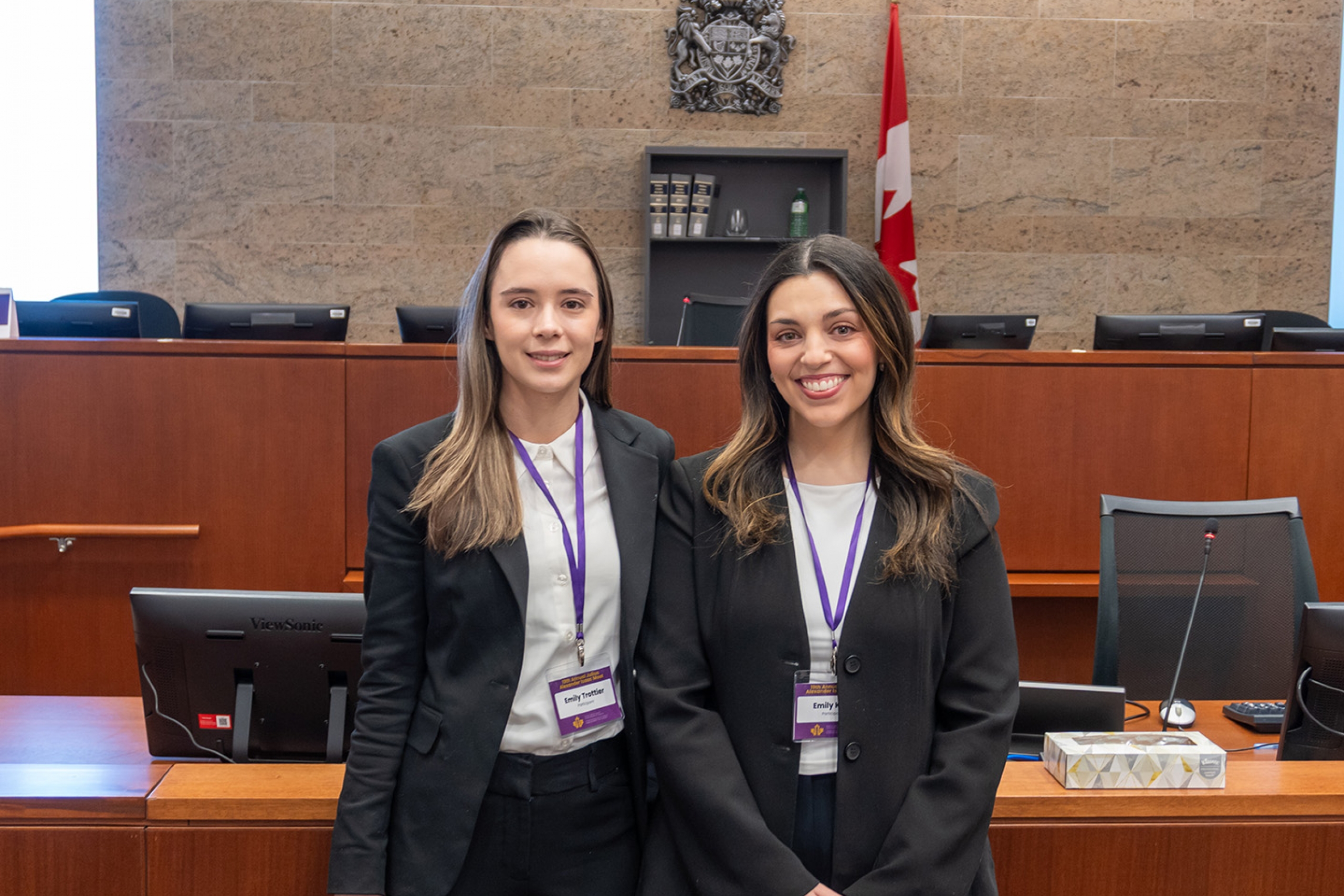 Two law students in suits pose in a wood and stone courtroom