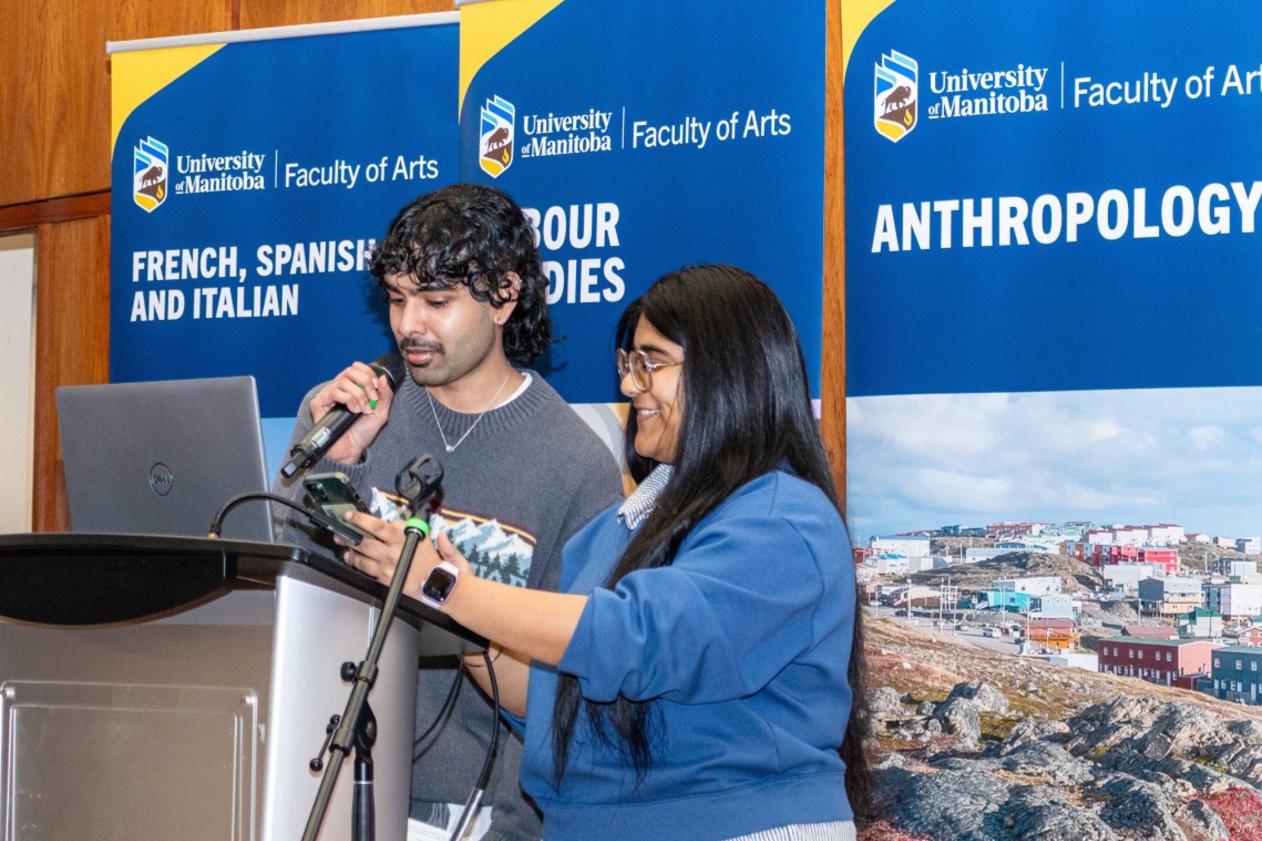Two students holding a microphone, standing at a podium on stage. 