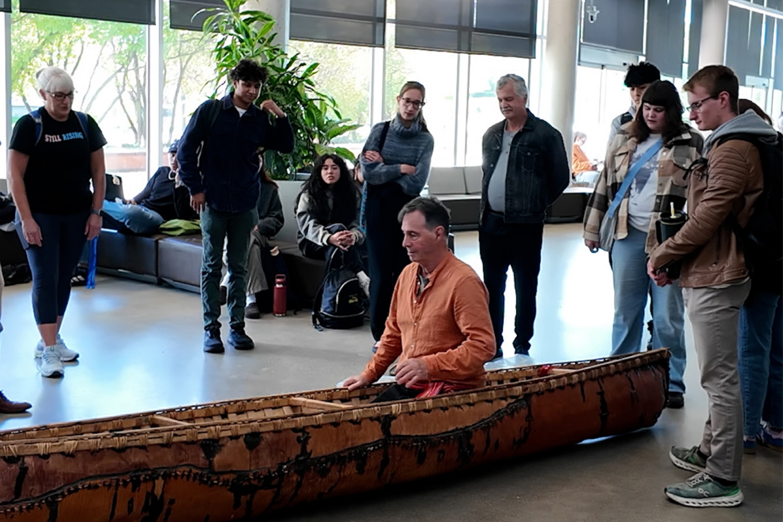 A man in an orange shirt demonstrate how the canoe can rock to a crowd of onlookers.