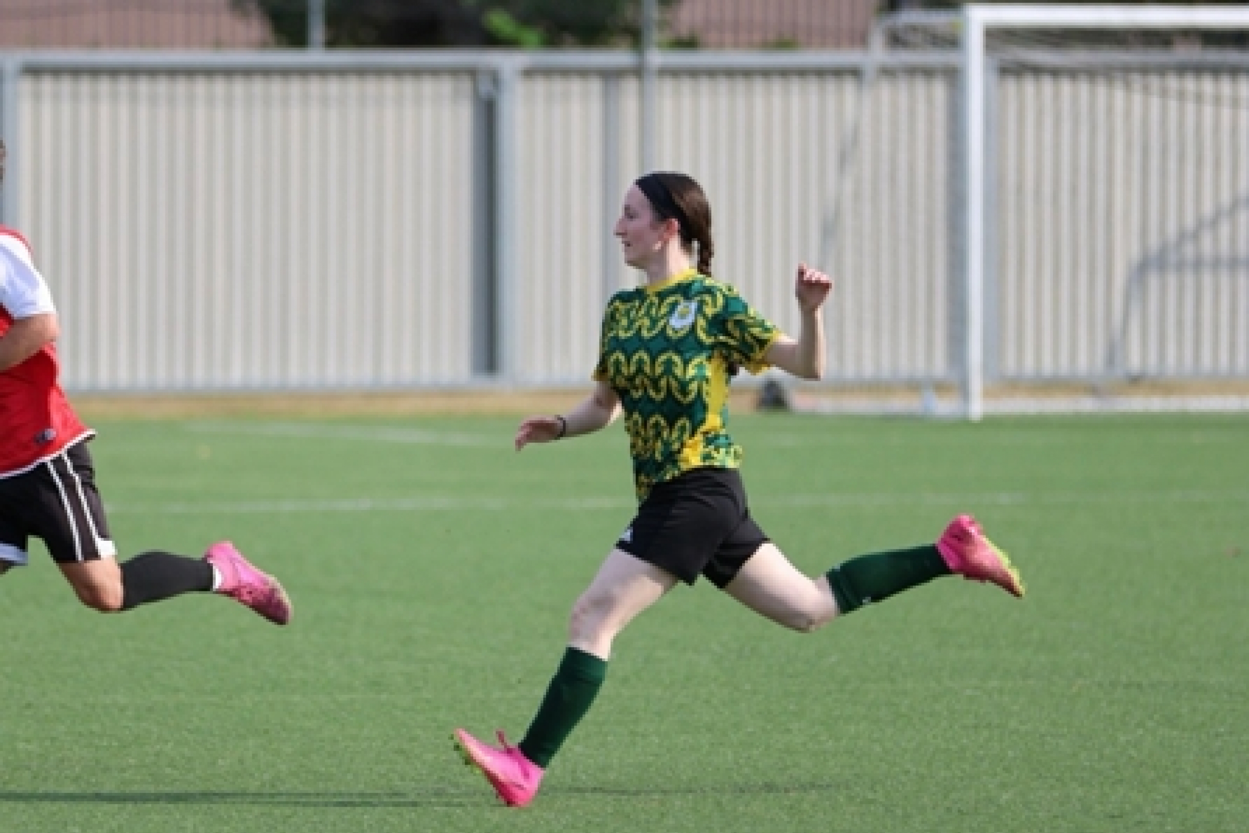A female soccer player captured midstride running across a soccer pitch.