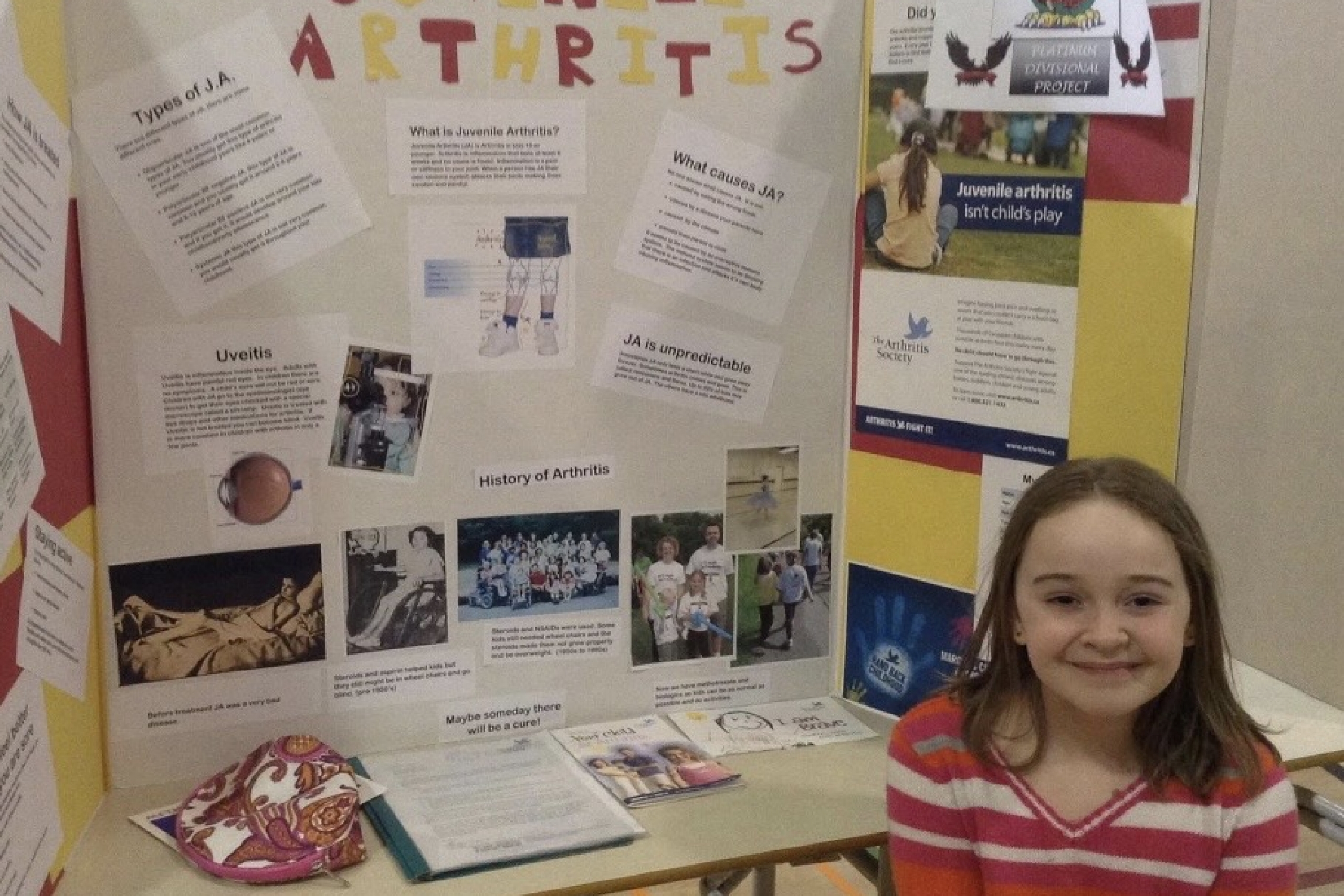 A young girl sits in front of she science fair booth where her poster reads: Juvenile Arthritis
