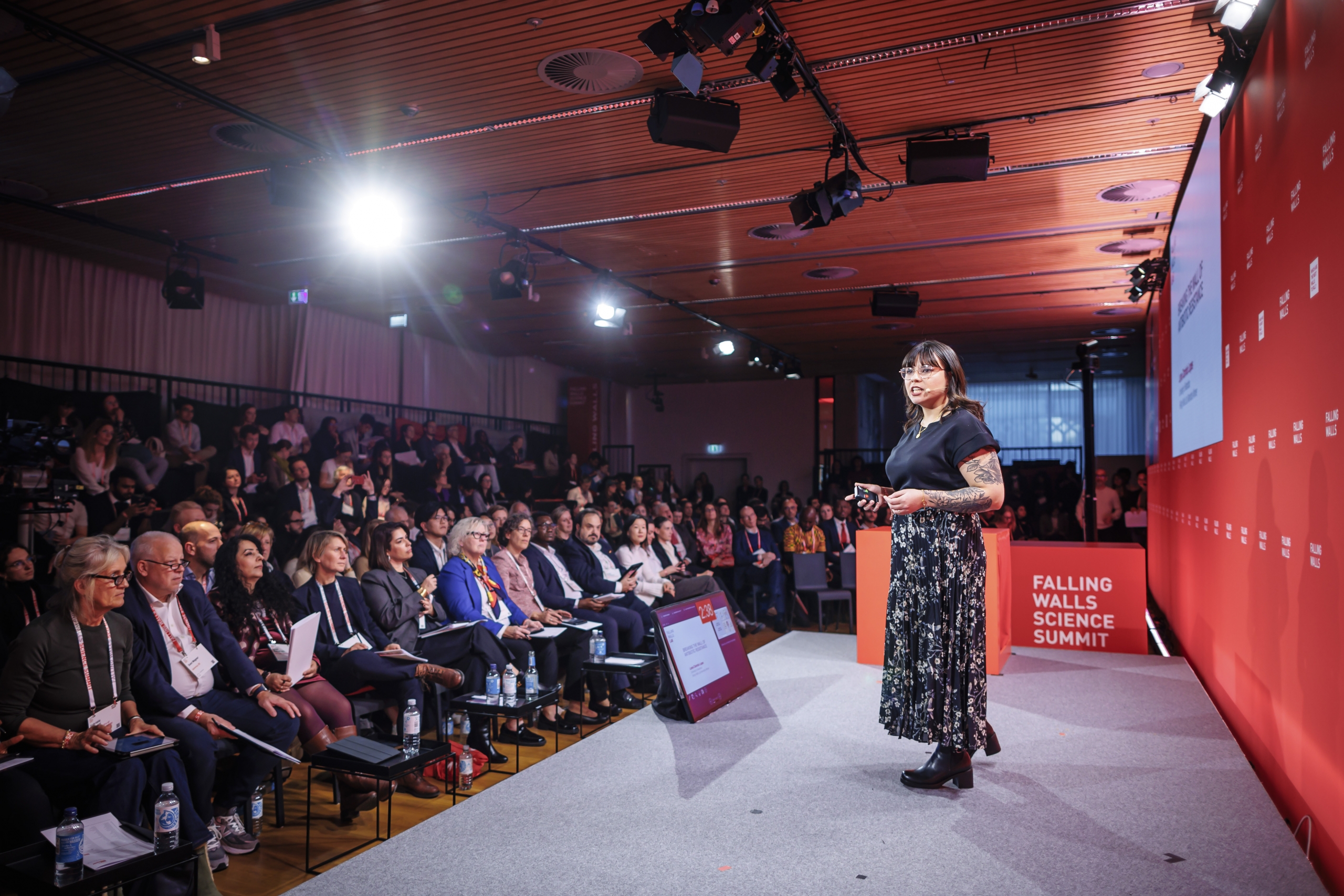 UoM student presents on stage at a Falling Walls Science Summit event, addressing a seated audience in a conference hall.