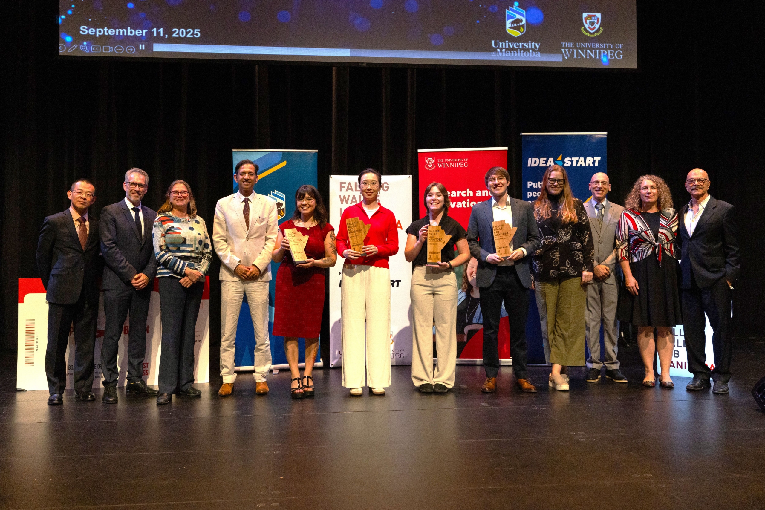 Falling Walls Lab Manitoba 2025 winners and organizers on stage with event banners.