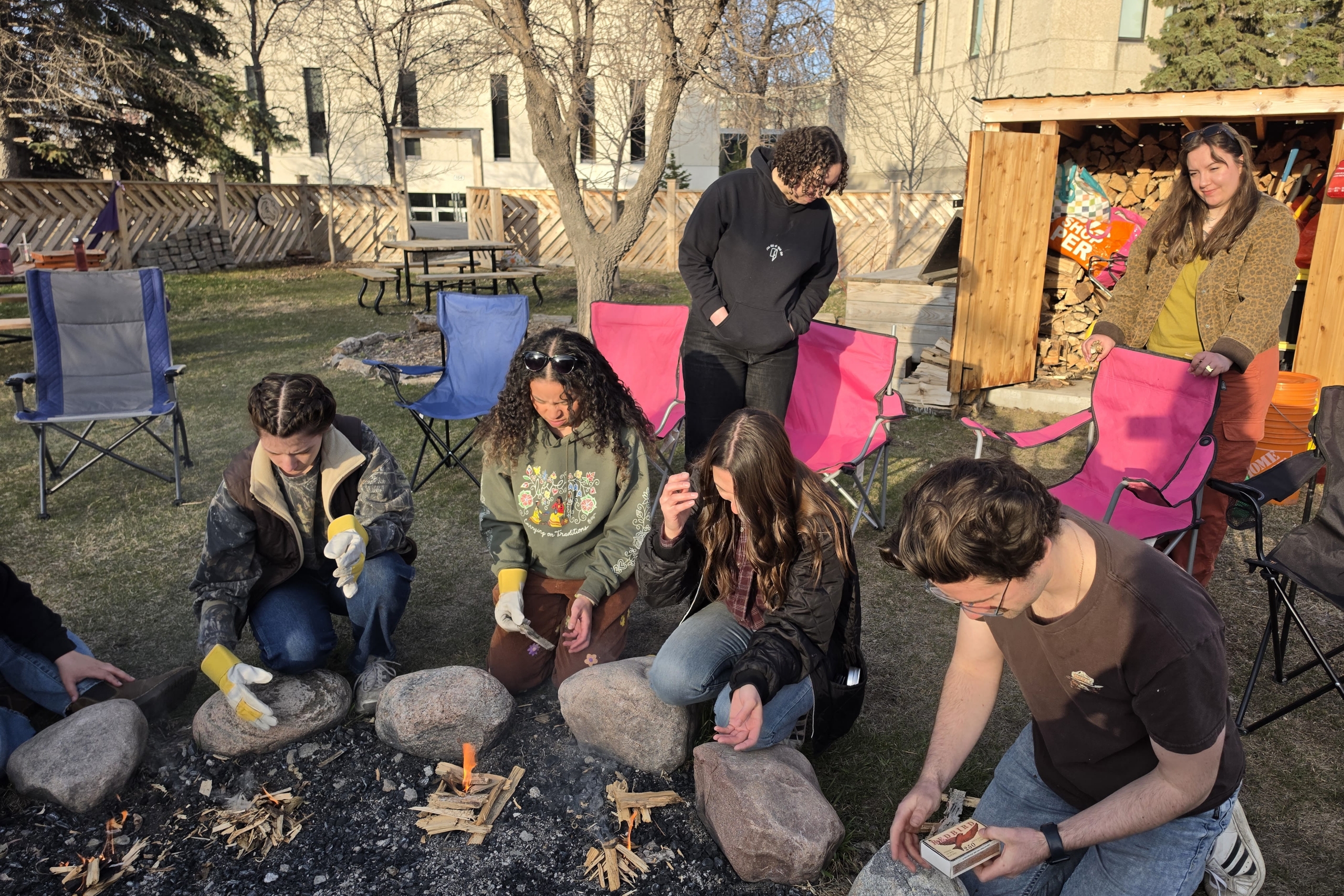 Four students kneeled over mini fires they've built outdoors.