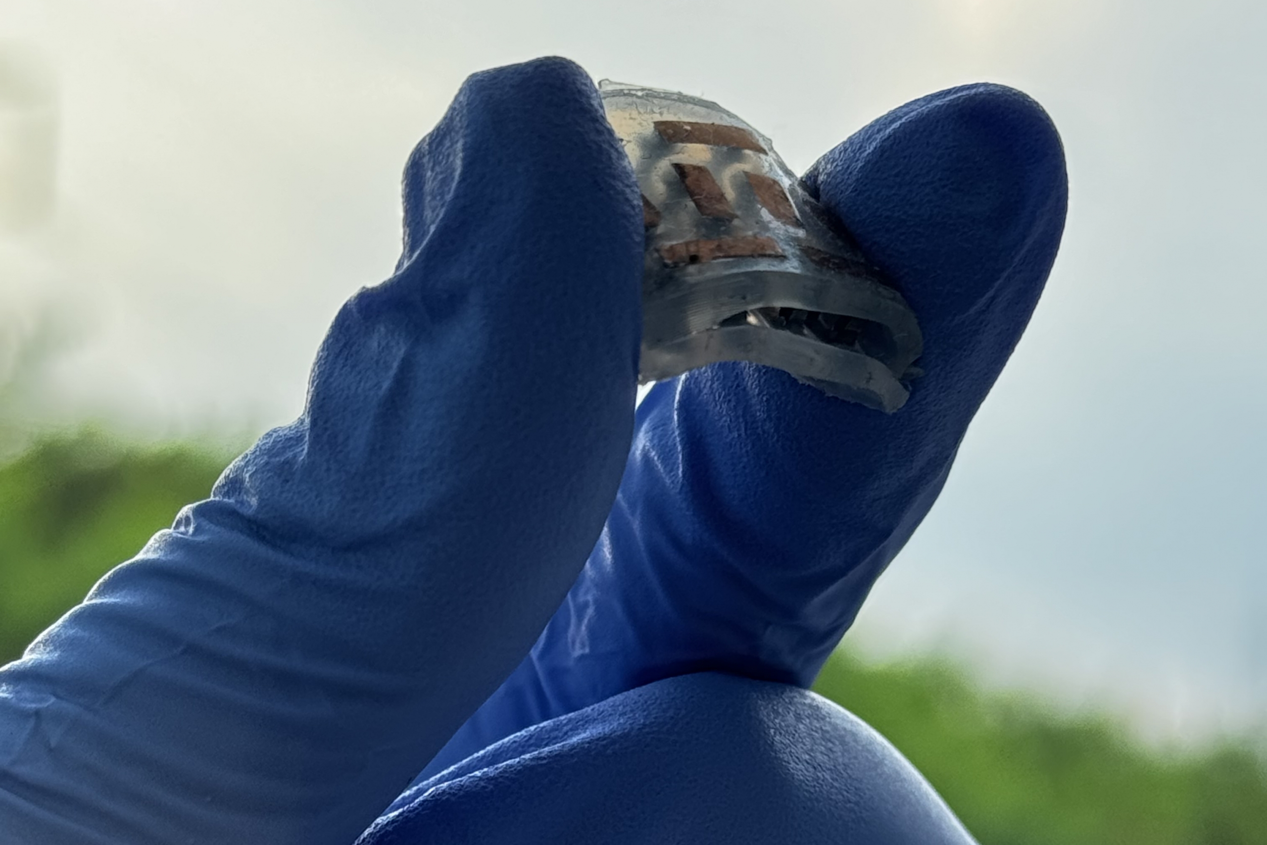 Gloved fingers hold a small device.