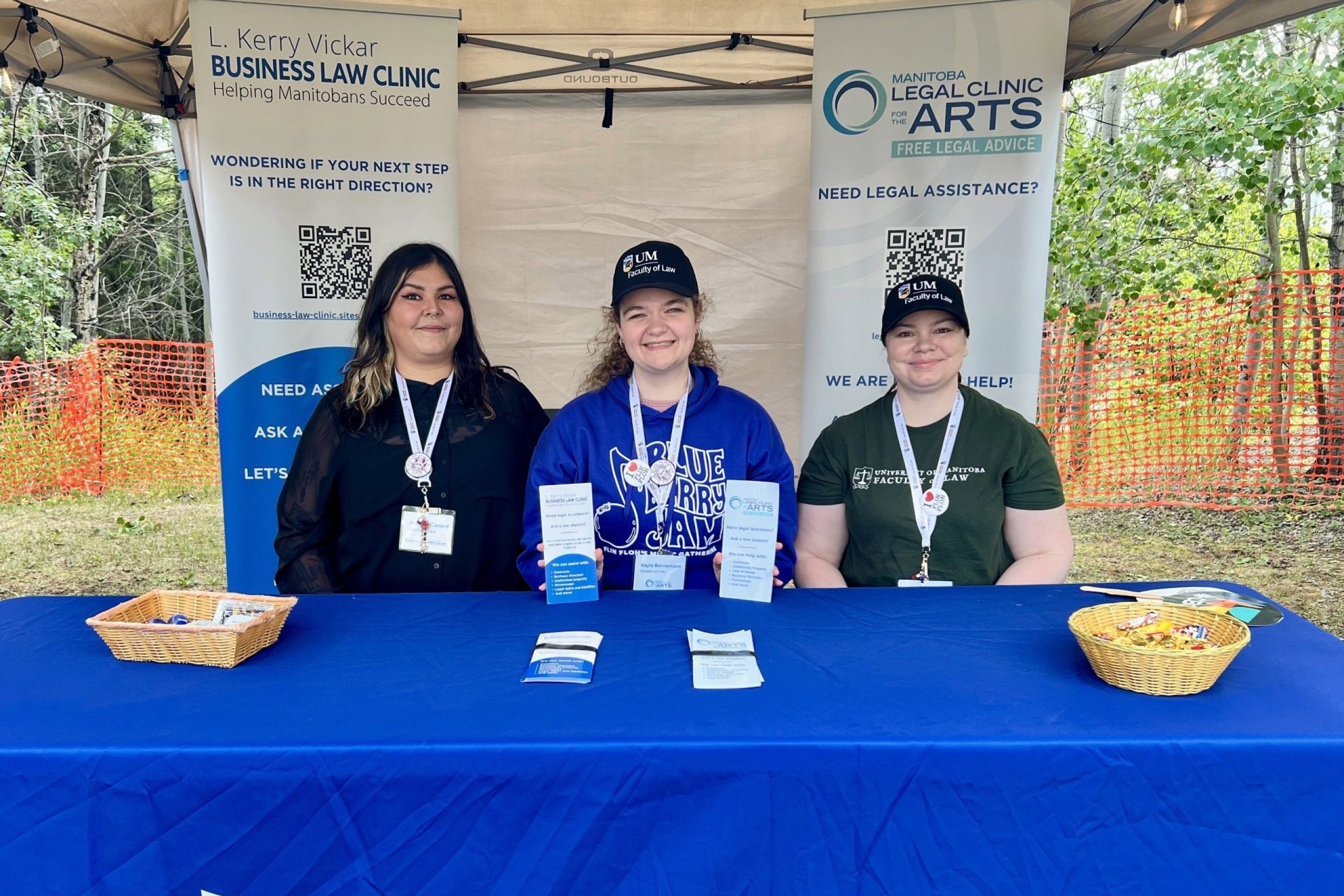 three women sit at a table covered with a blue UM Faculty of Law cloth at a tradeshow