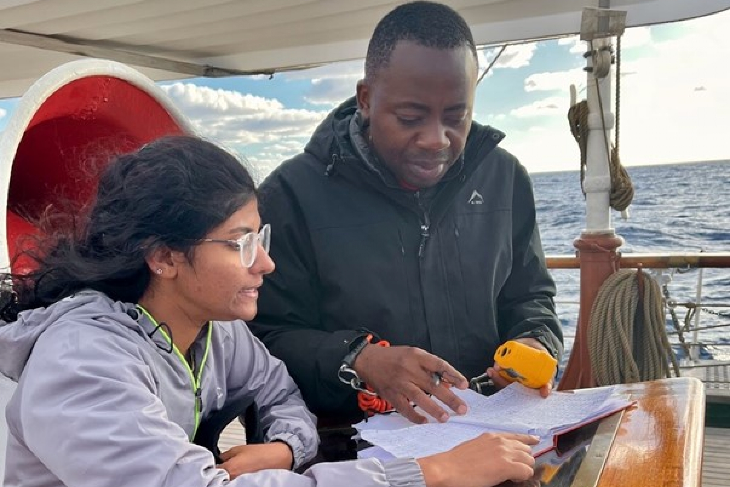 Franck Ghomsi reviewing a map with a colleague on a boat in the water.