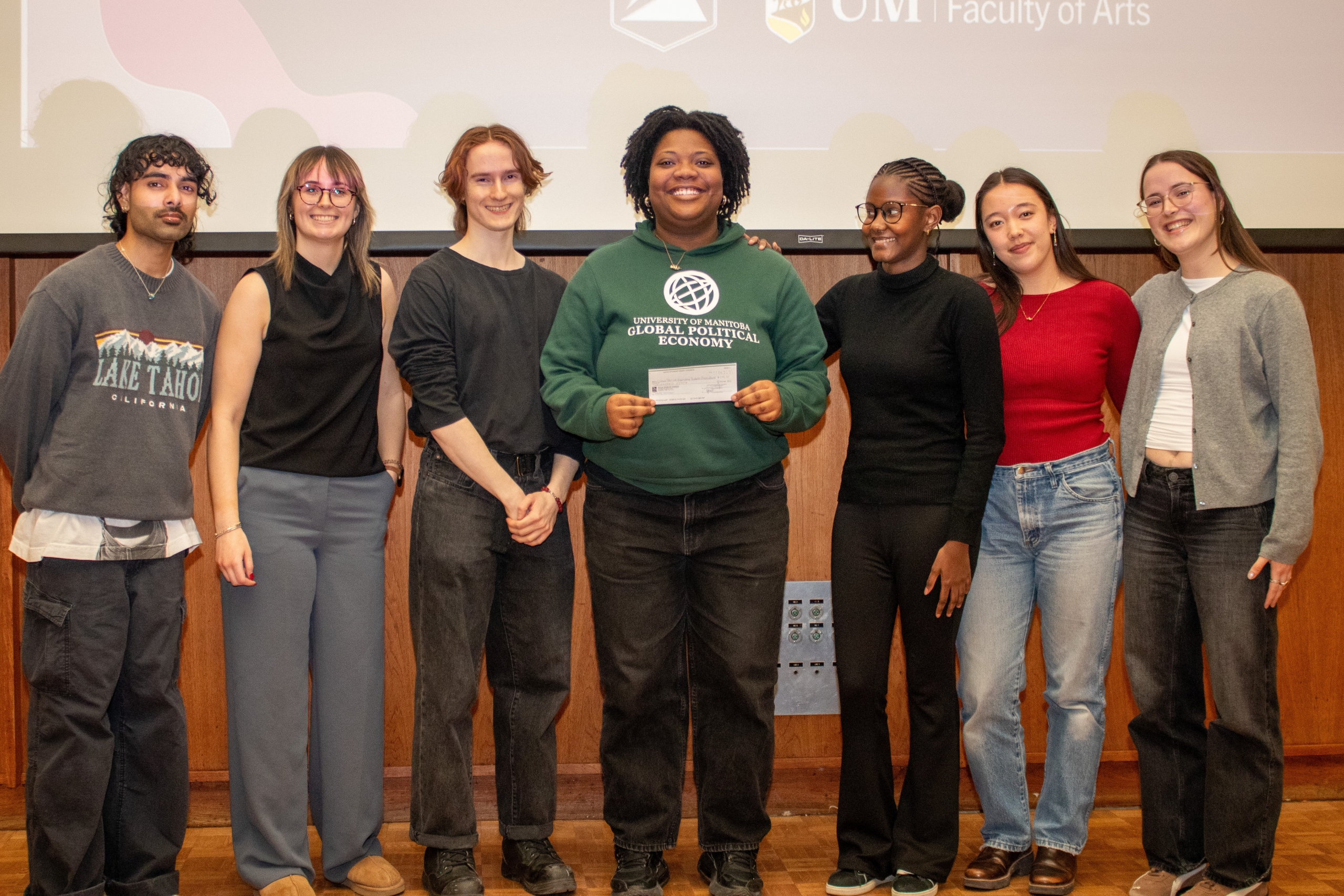 A group of 7 students standing together, one is holding up a winning certificate.