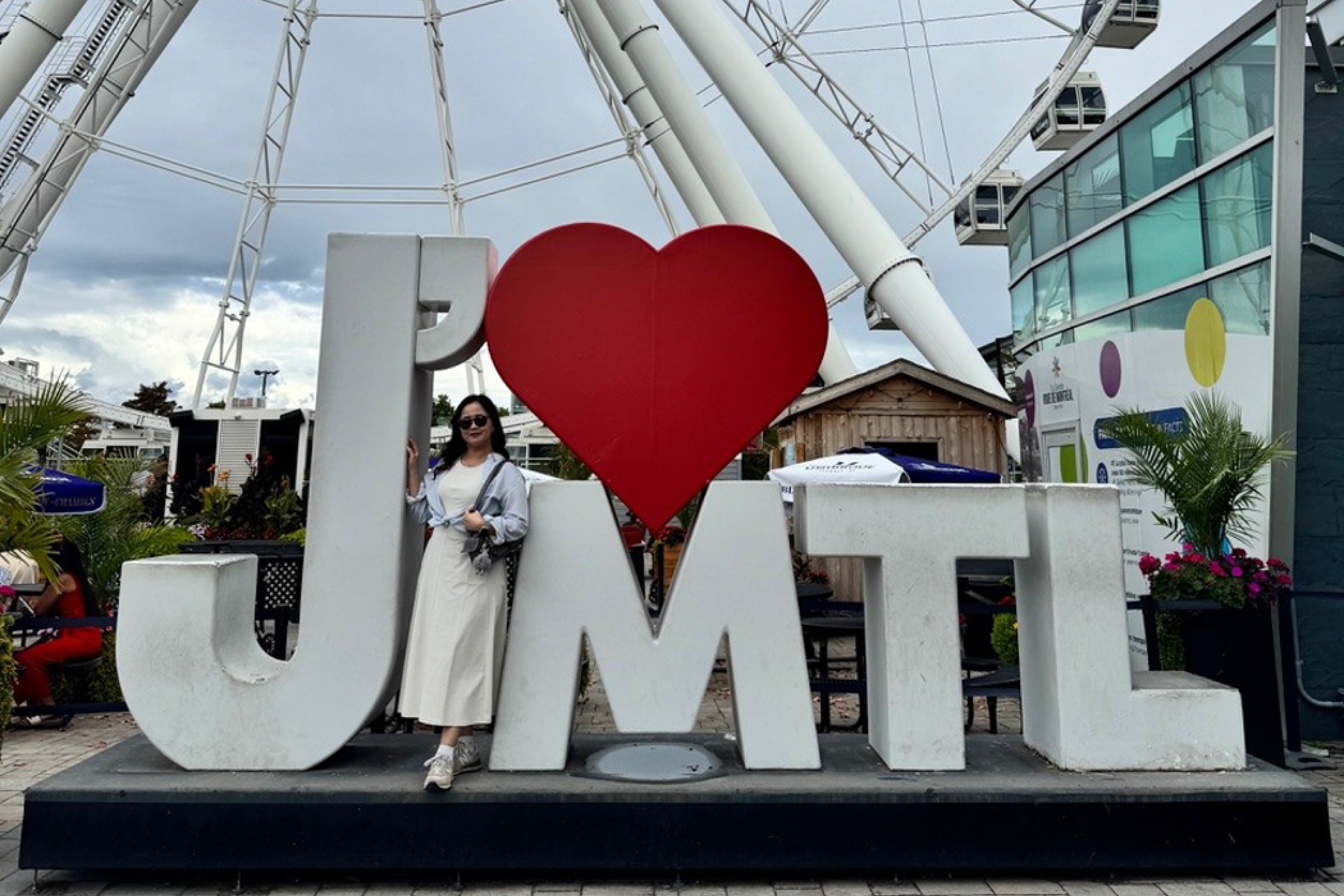 Gloria Lee standing beside a J’ ❤️ MTL sign with a ferris wheel in the background.