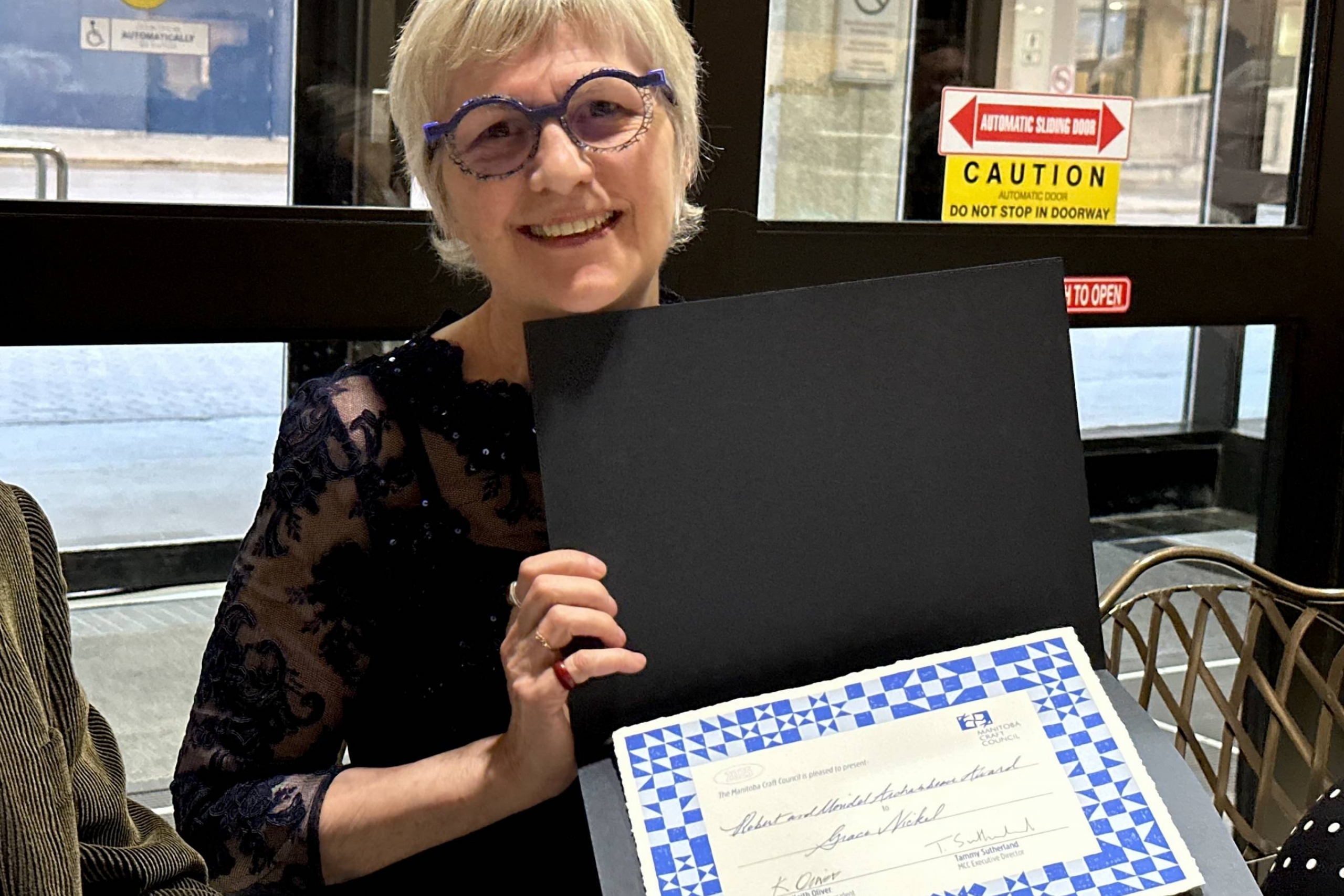 Grace Nickel smiles while holding her Inaugural Archambeau Award of Distinction certificate.