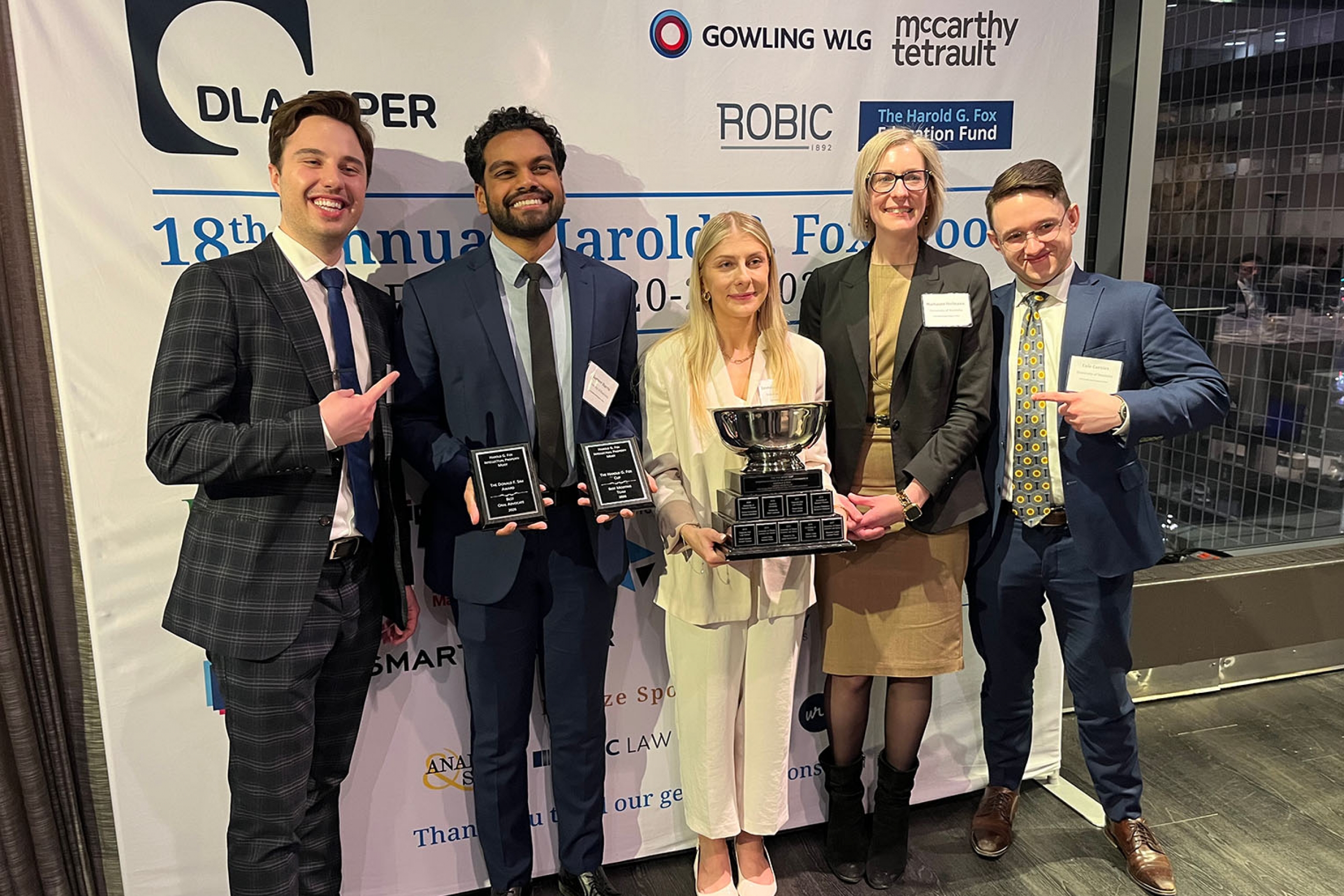 five law students hold a large trophy and two awards plaques