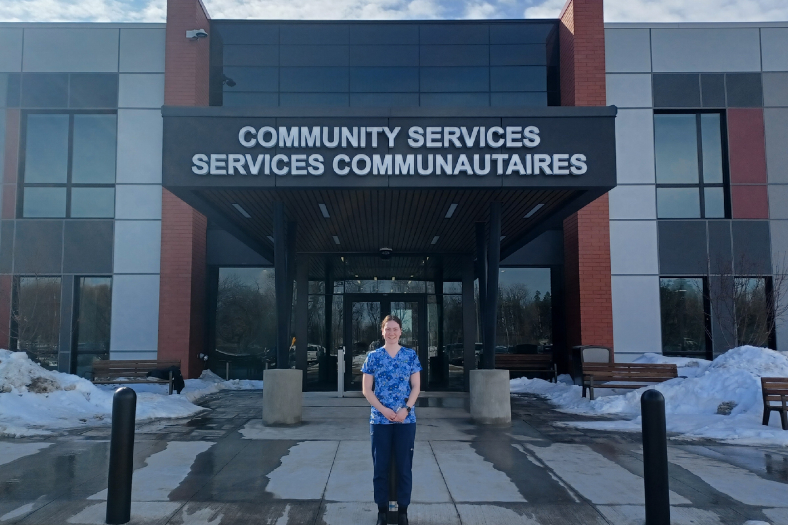 A person stands in front of a building exterior. The building sign says "Community Services, Services Communautaires".