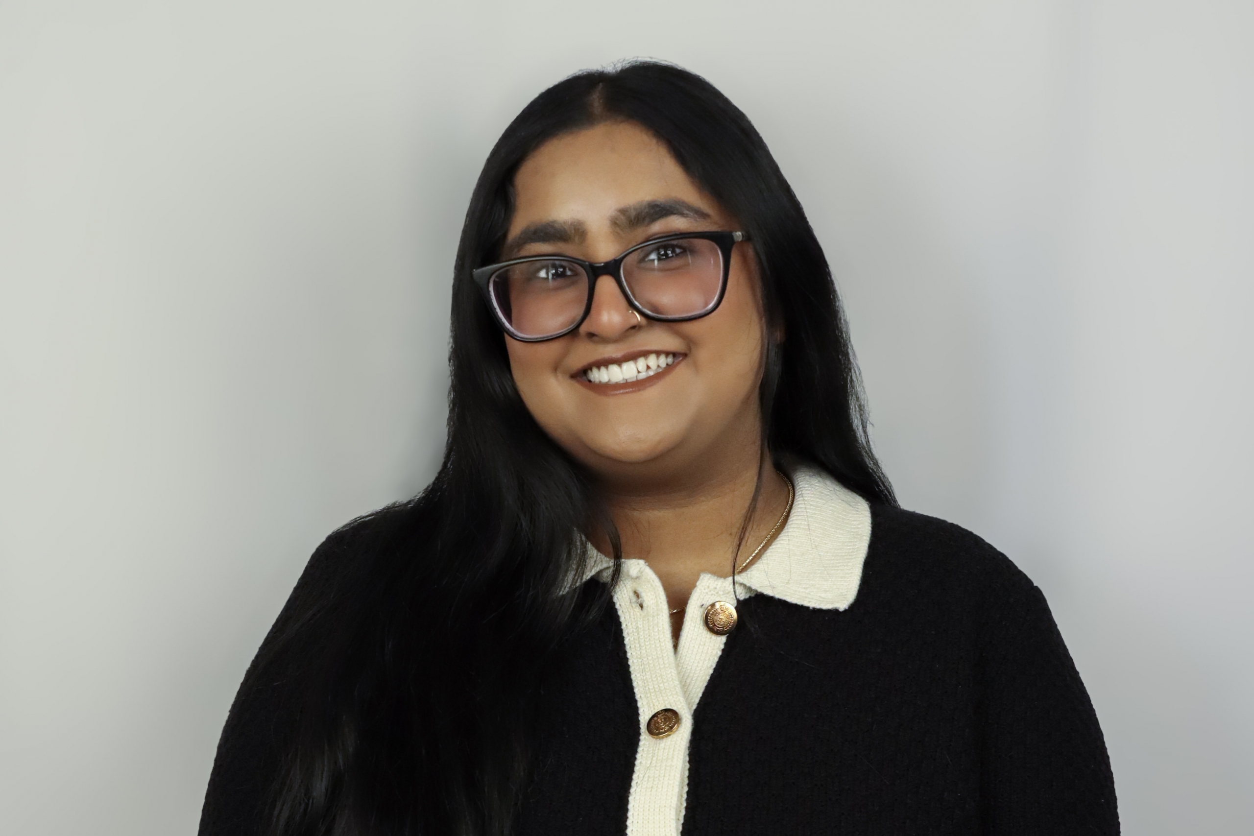 person with dark hair and glasses wearing white shirt and dark jacket