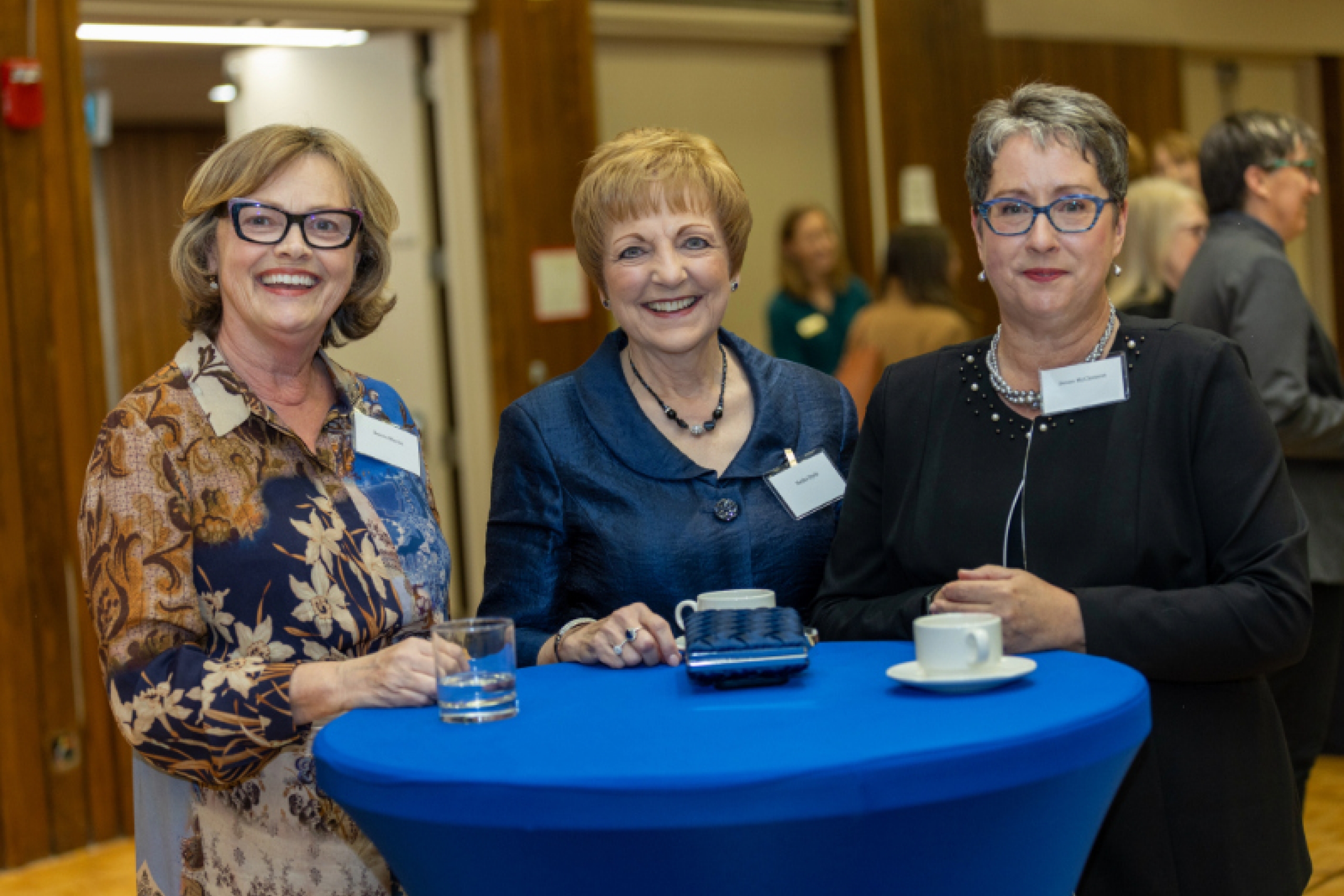 three women smile, standing around a banquet table