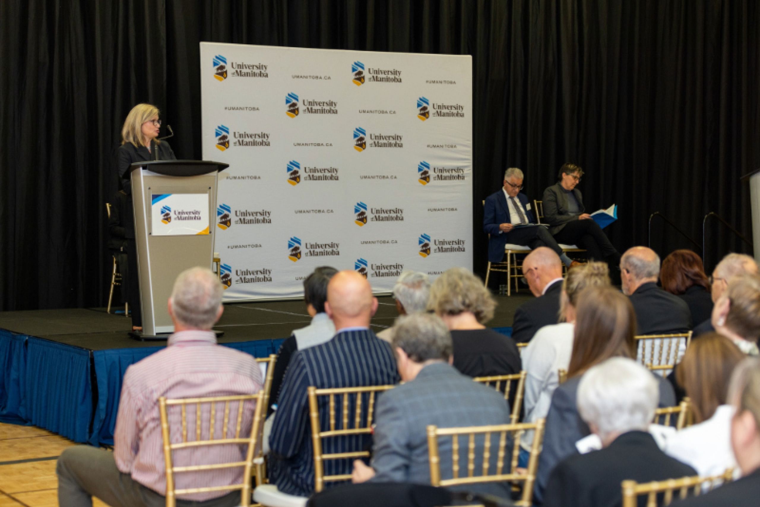 Chancellor Anne Mahon stands at the podium in front of guests.