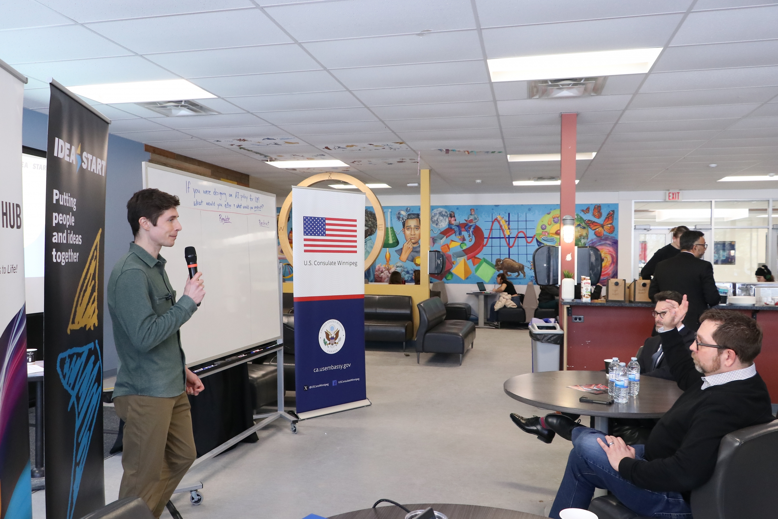 A facilitator leads an interactive whiteboard session at IDEA START with participants seated nearby.