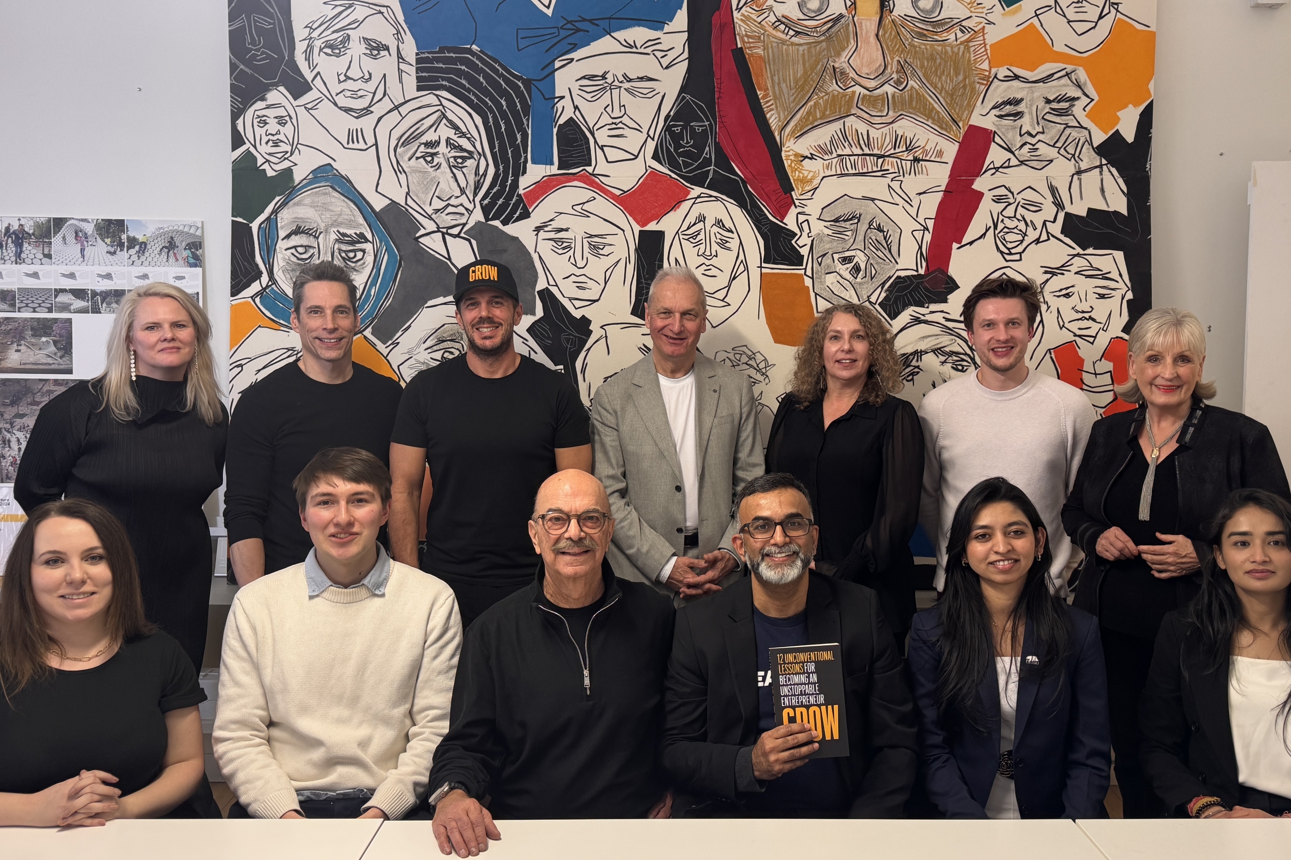 IDEA START Advisory Board and team members posing indoors in front of a large mural, with several seated and others standing behind.
