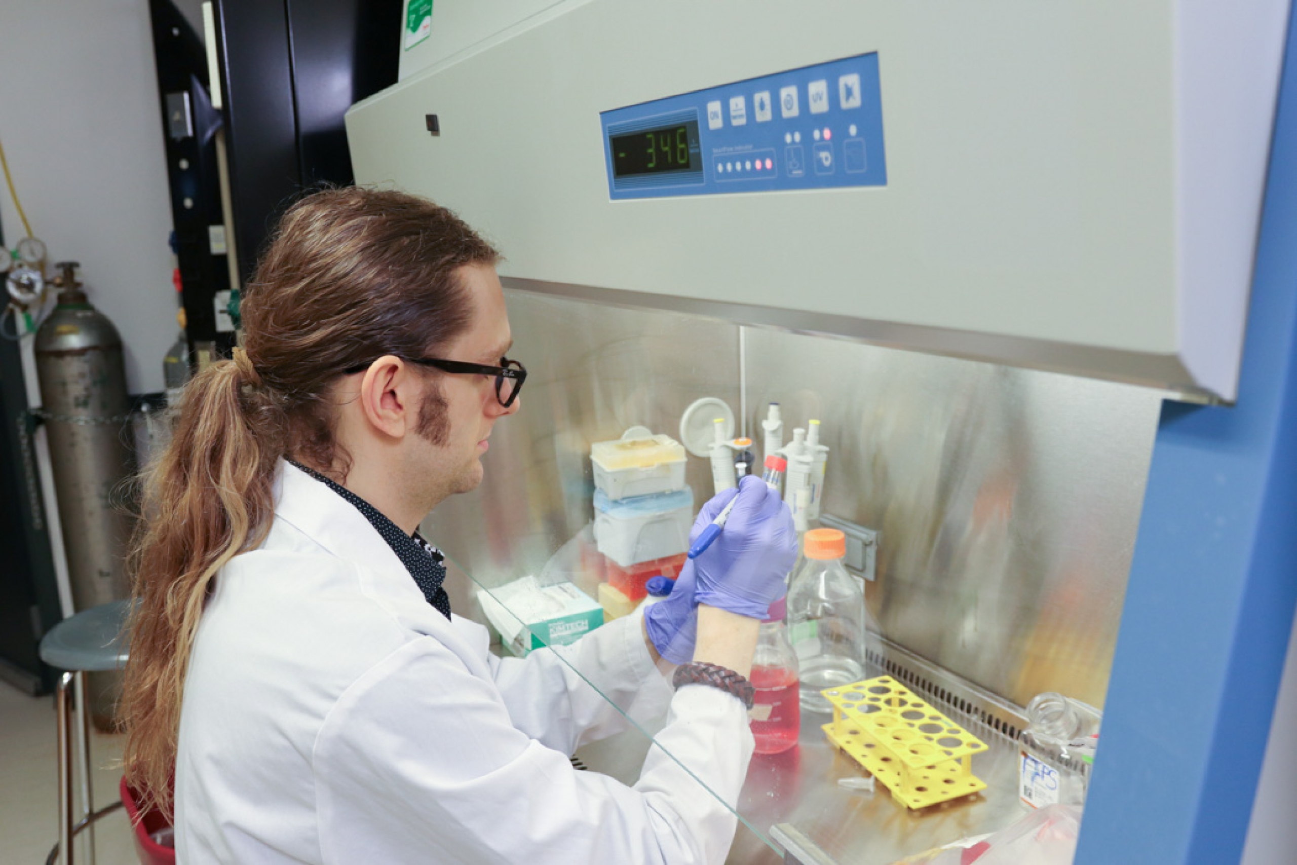 Eli Mondor labels a test tube while seated in a lab, with scientific equipment visible in the background.